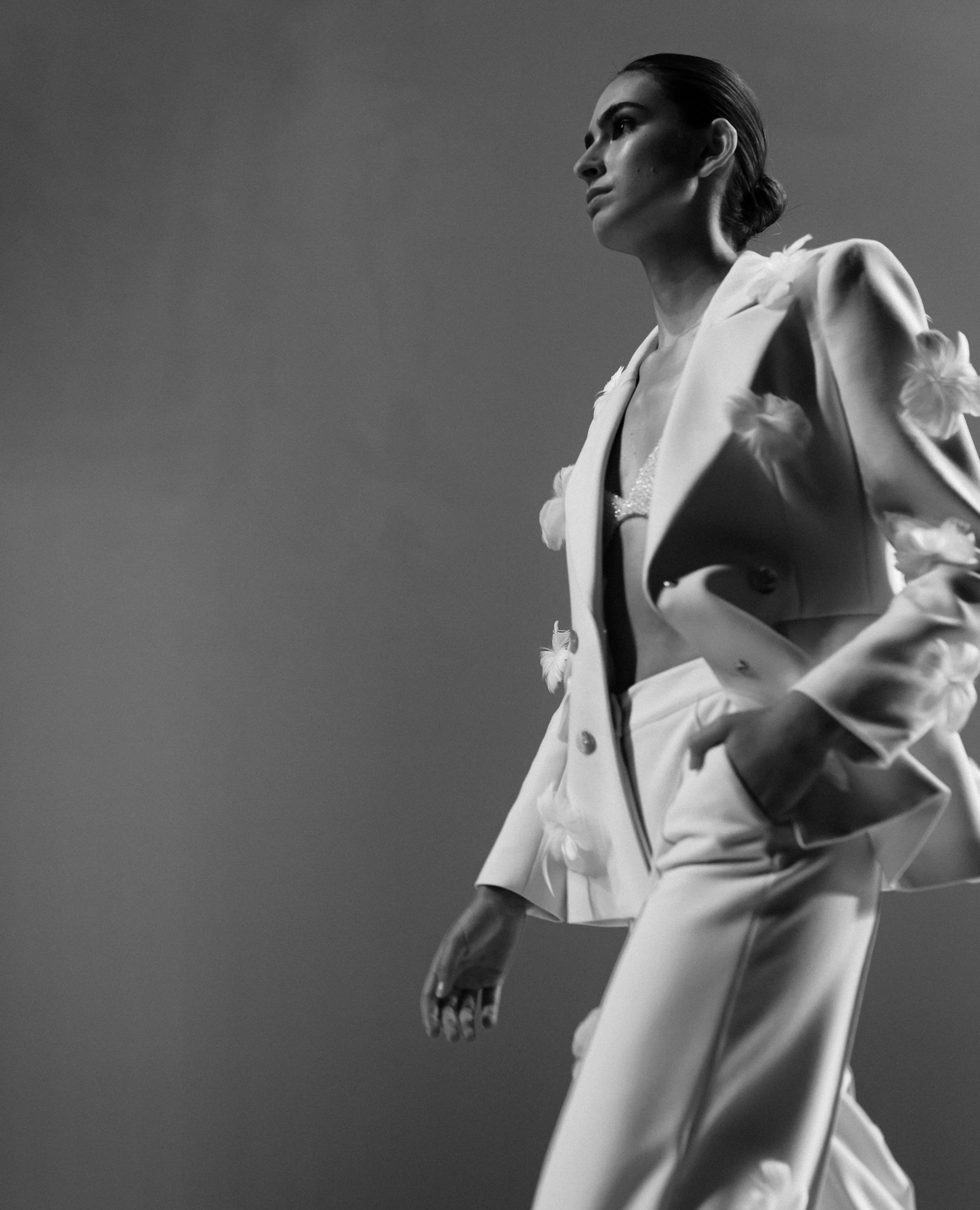Black and white photo of a woman in a suit with feather details, standing with a confident pose against a plain background.