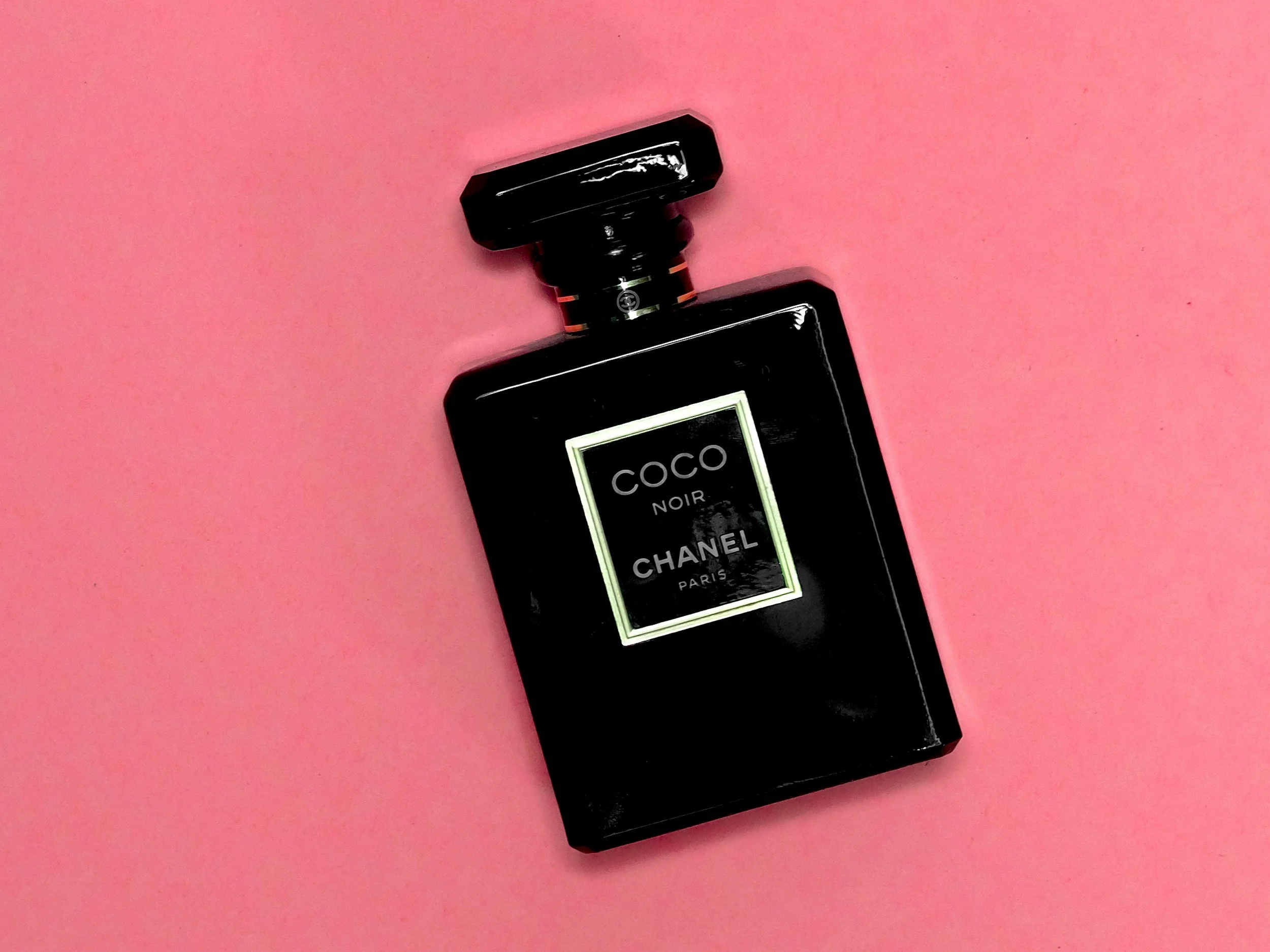 Black Chanel Coco Noir perfume bottle on pink background.