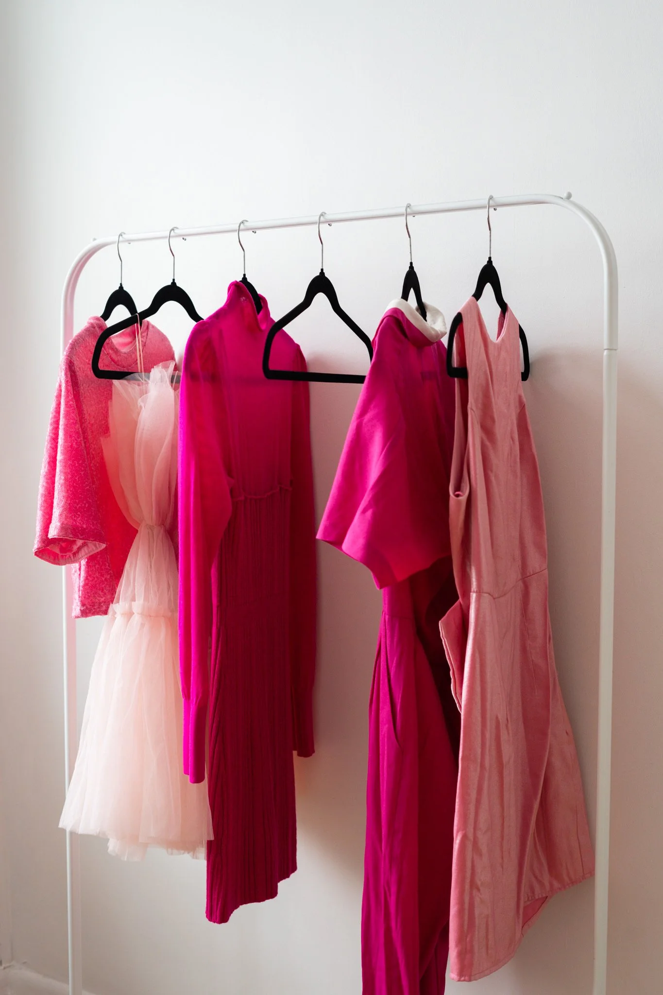 Various pink and peach clothing items hanging on a white clothing rack, including dresses, tops, and pants.