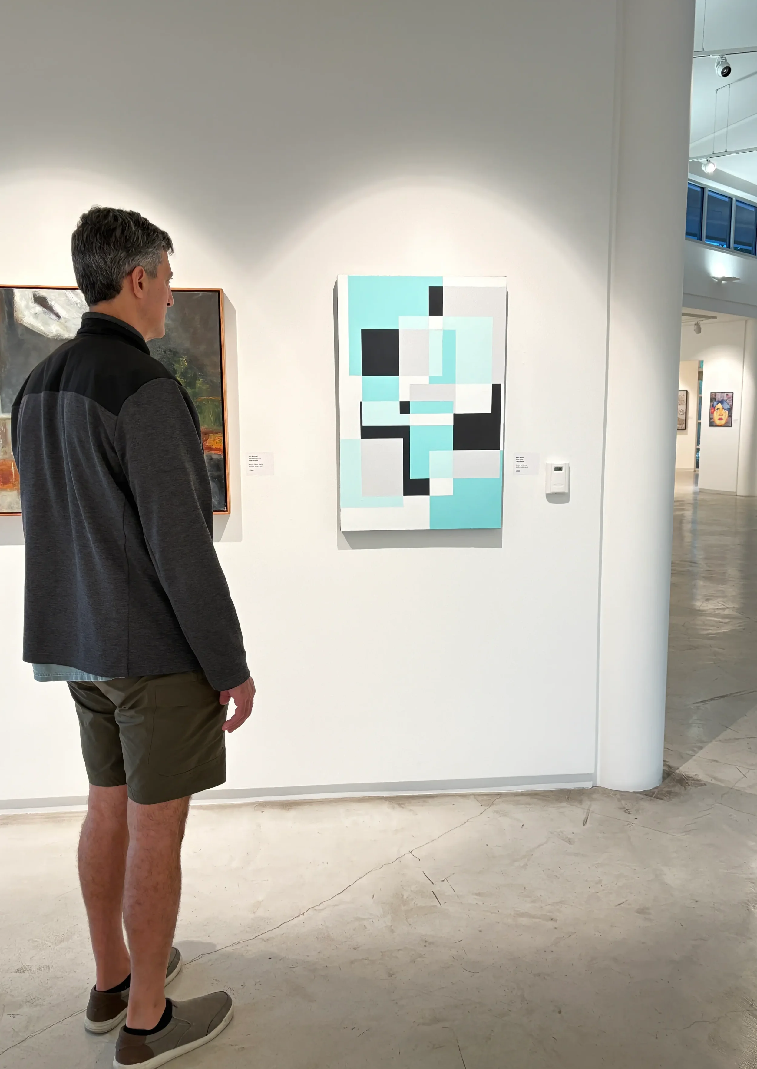 A man observing an abstract geometric painting with blocks of black, white, light blue, and gray in an art gallery.