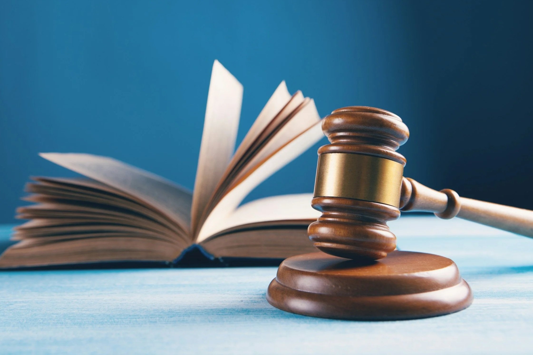 Judge's gavel in front of an open law book on a blue surface.