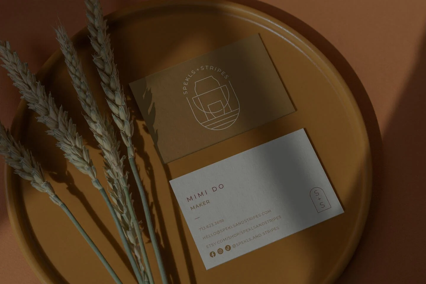 Business cards and dried wheat stalks on a round wooden tray.