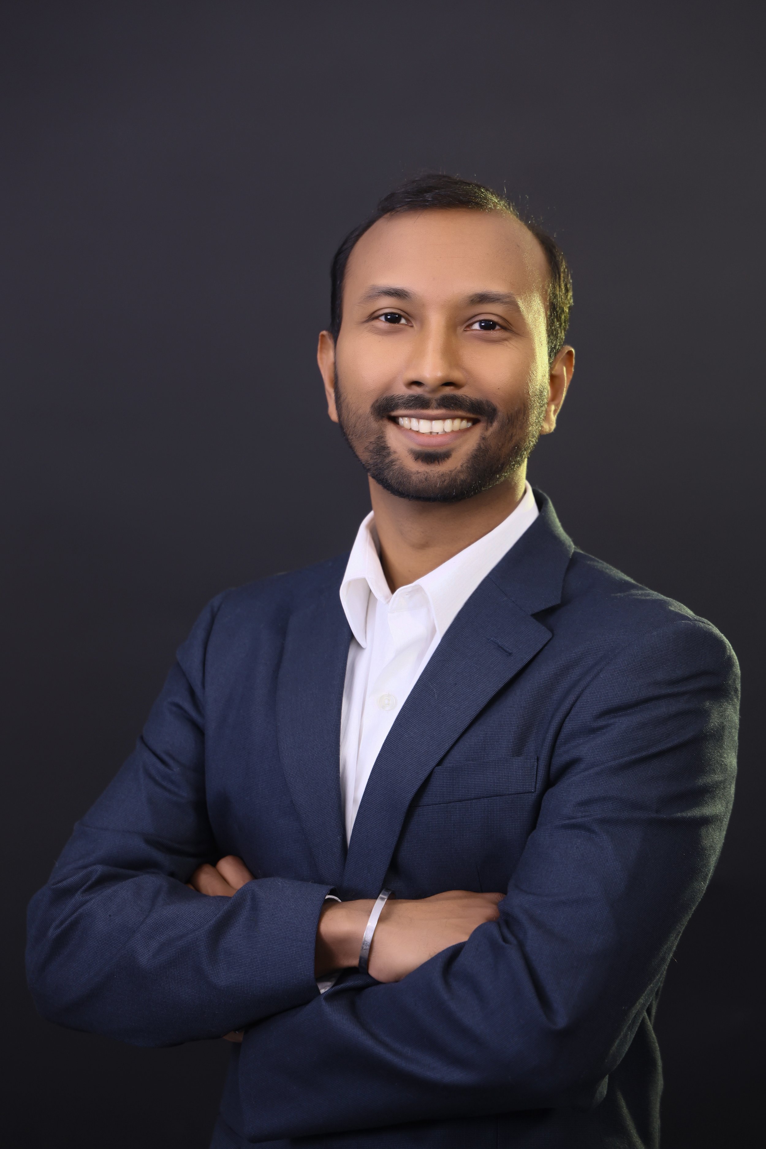 Professional portrait of a smiling man with crossed arms, wearing a navy blazer and white shirt, against a dark background.