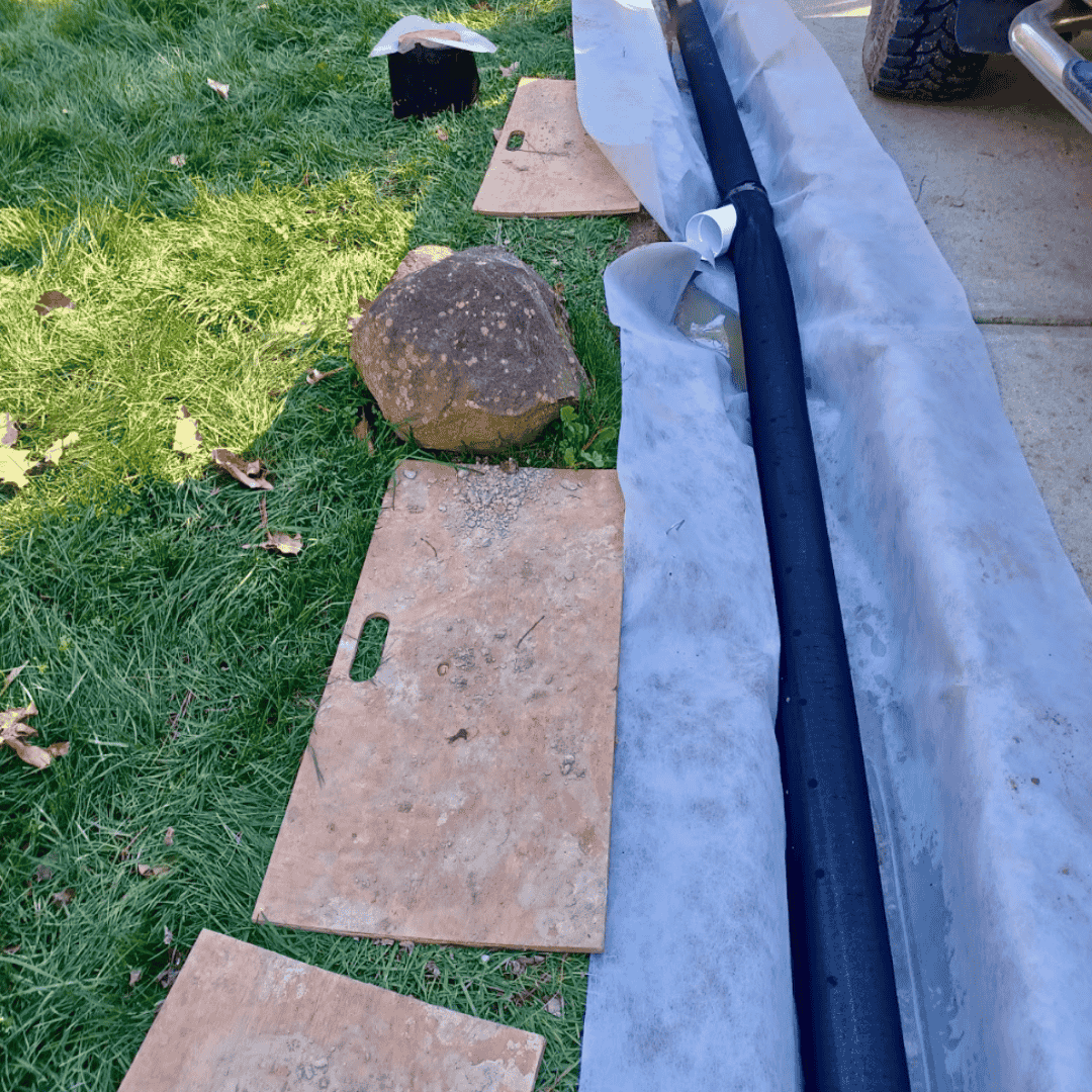 Residential drainage worksite beside brick pavers with protective tarp and piping—non-invasive yard drainage installation in Pittsboro, NC.