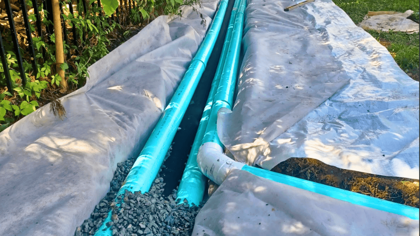 Solid PVC drainage pipe installed in a gravel trench with protective sheeting—non-invasive yard drainage work in Cary, NC.