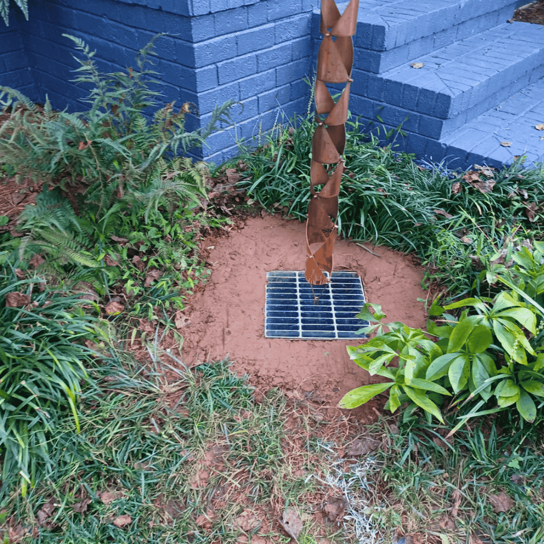 Low-profile yard drain inlet near home steps in a landscaped bed—runoff drainage solution for a residential property in Chapel Hill, NC.