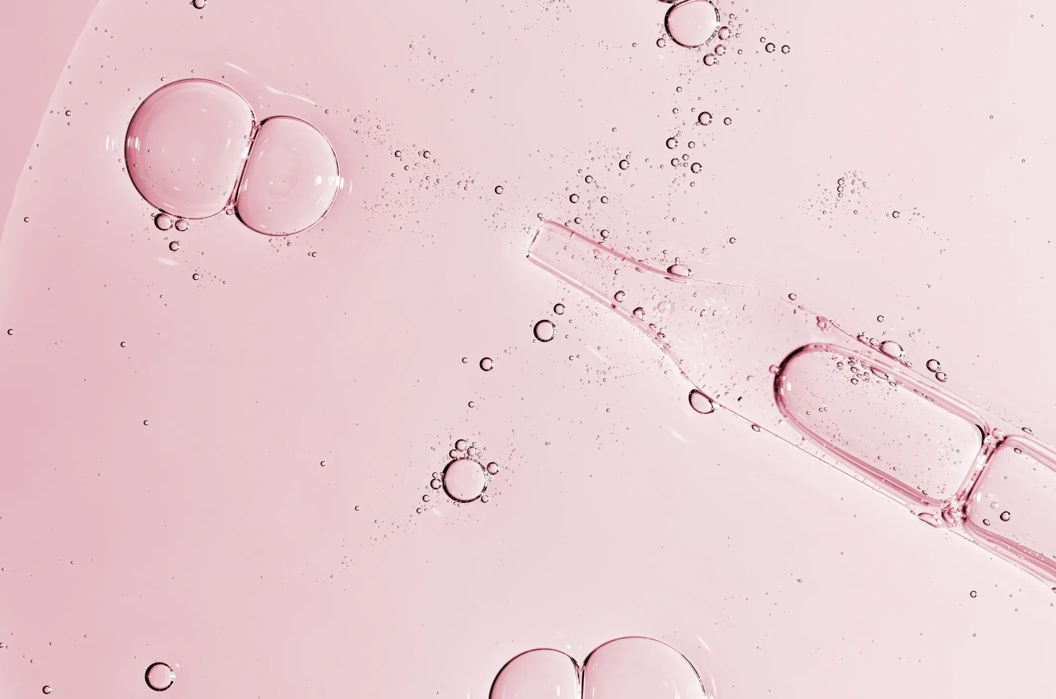 Niacinamide serum texture with suspended air bubbles on a pink background.