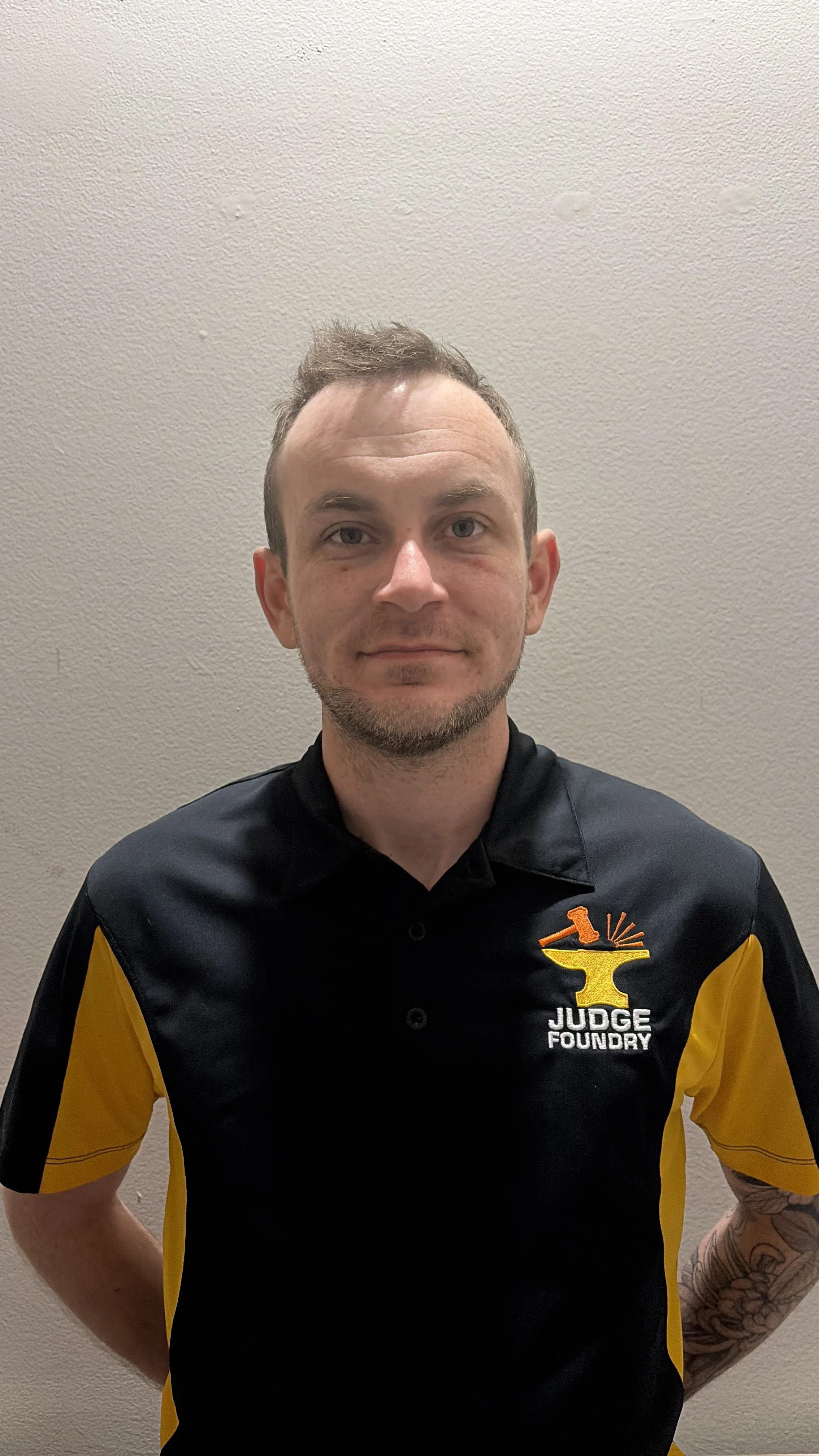A man wearing a black and yellow shirt with a logo and the text 'Judge Foundry,' standing against a plain wall.