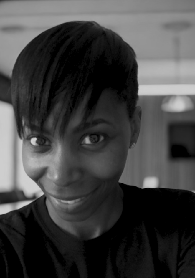 A smiling woman with short hair taking a selfie indoors, in black and white.