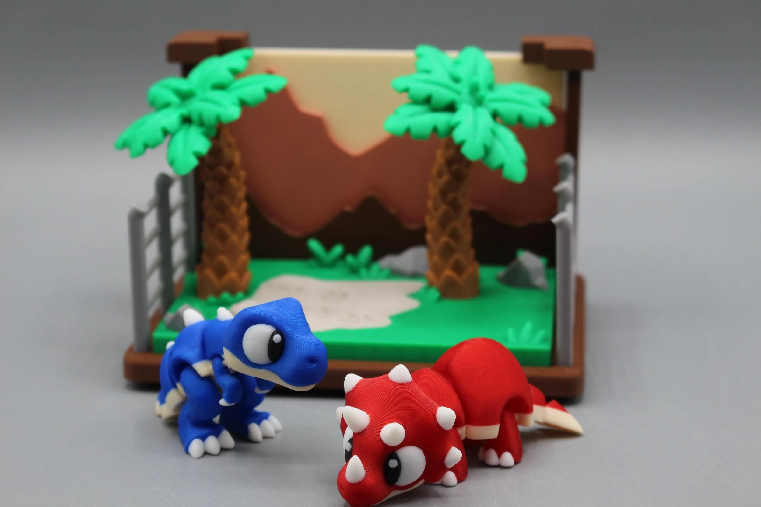 Colorful toy dinosaurs in front of a miniature jungle scene with palm trees and rocks.