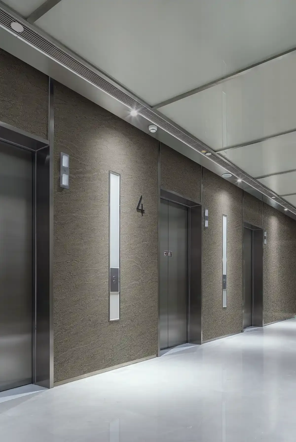 Four elevator doors in a modern building hallway, numbered 3 and 4, with sleek metallic finishes, illuminated panels, and minimalist design.