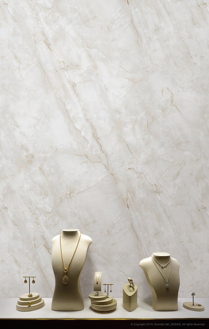 Display of jewelry including necklaces, earrings, rings, and bracelets on beige stands and platforms in front of a marble wall.