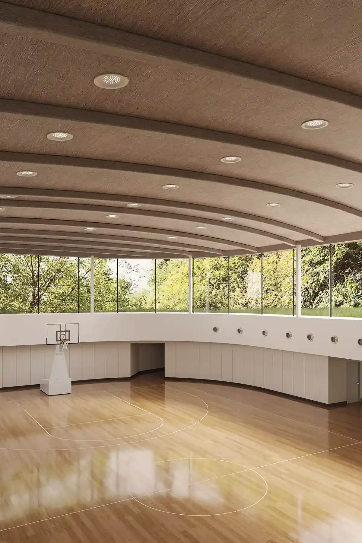 Empty indoor basketball court with wooden flooring, basketball hoop, and large windows showing trees outside.