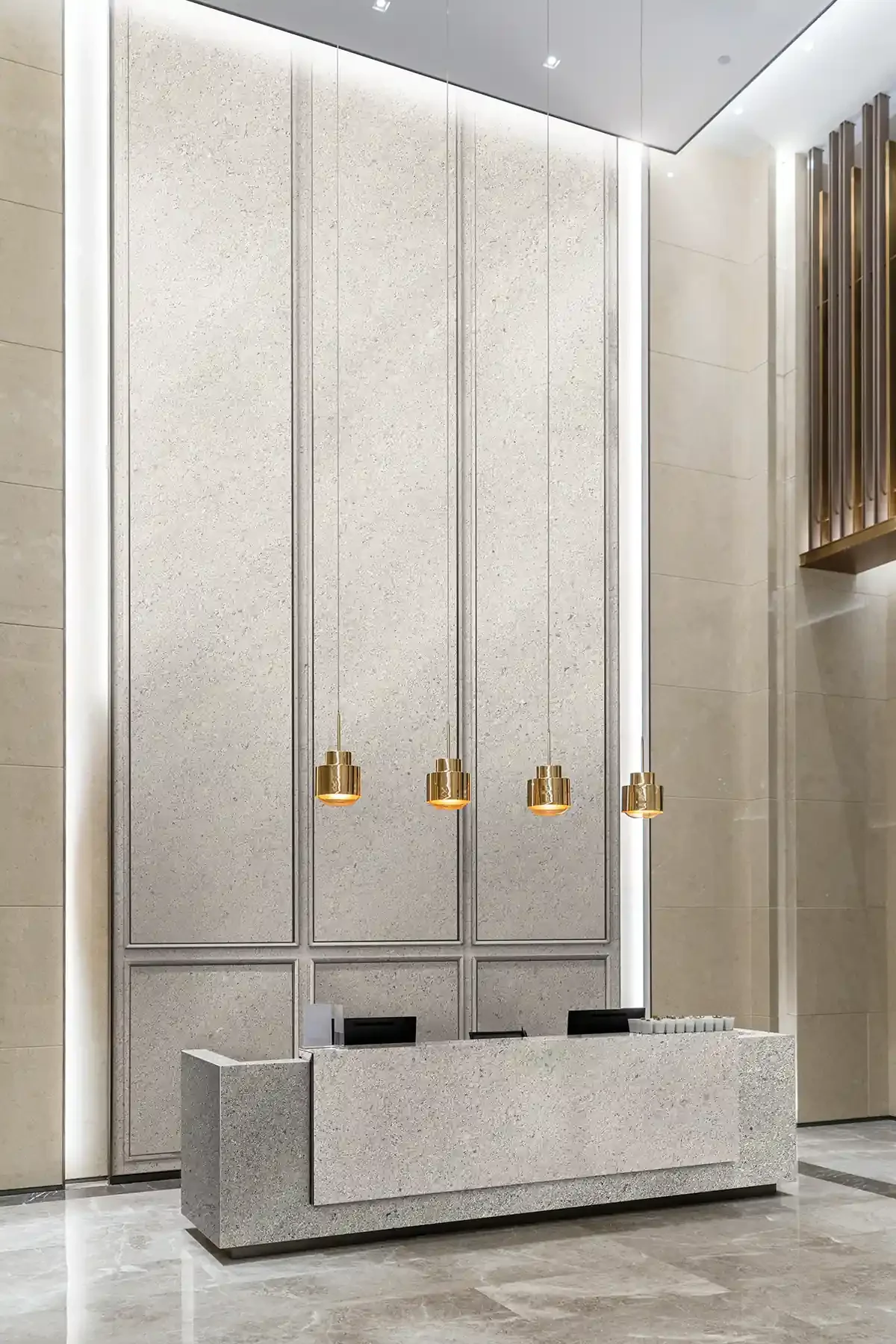 Modern lobby reception desk with textured beige wall panels, four gold pendant lights, and marble flooring.