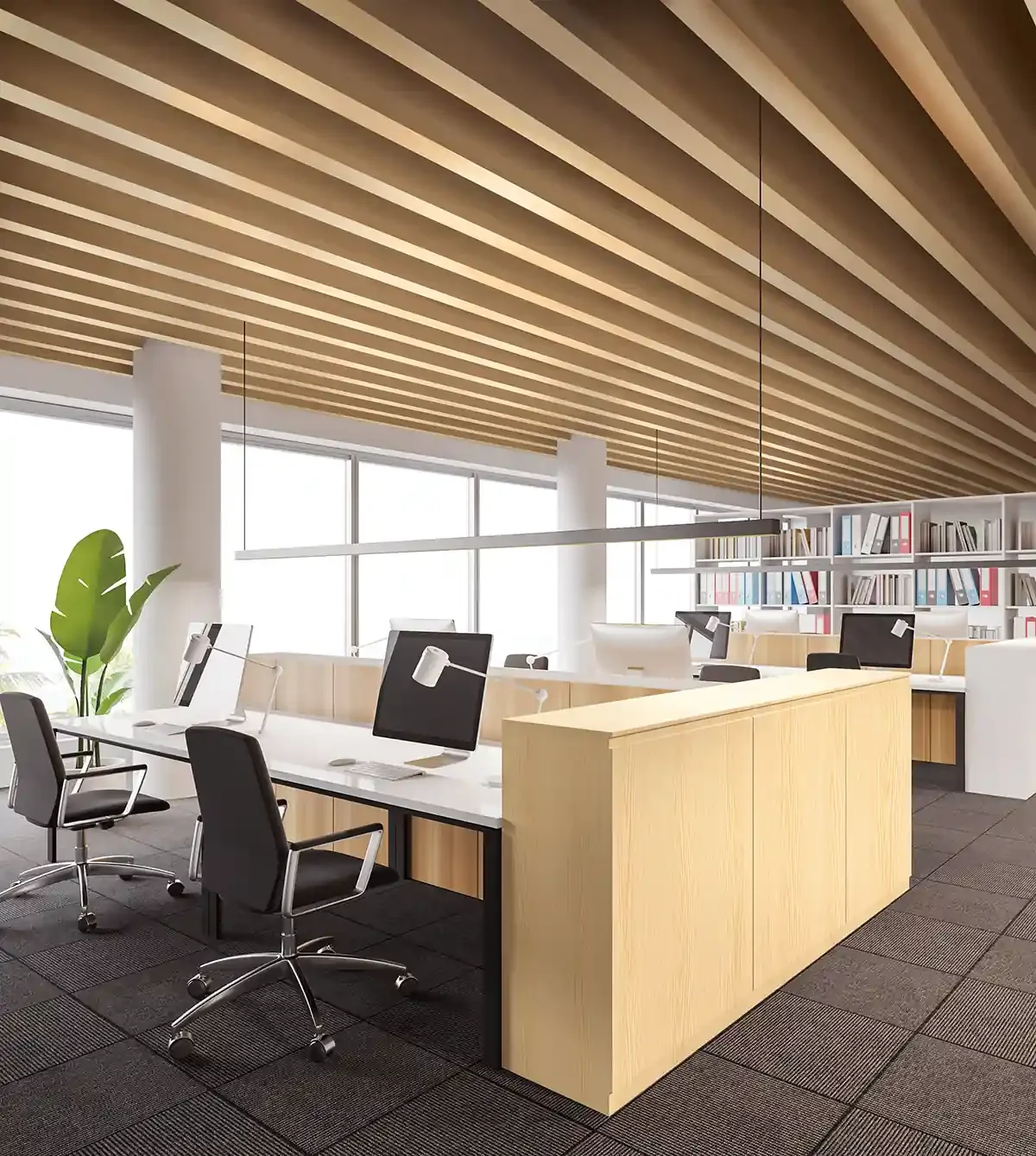Modern office with workstations and computers, wooden ceiling, large windows, bookshelves, and potted plant.