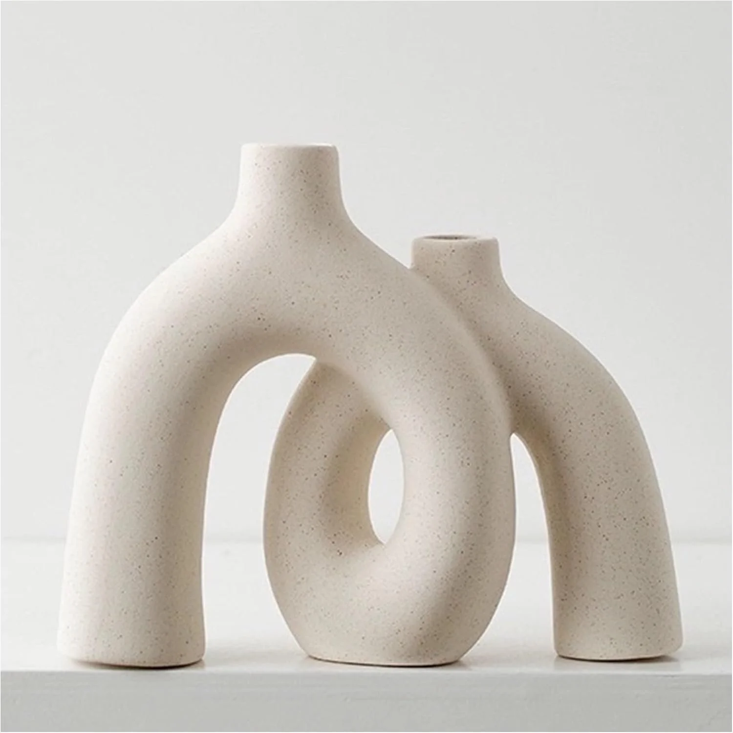 Minimalist cream-colored ceramic sculpture with three interconnected arch shapes on a white surface against a white background.