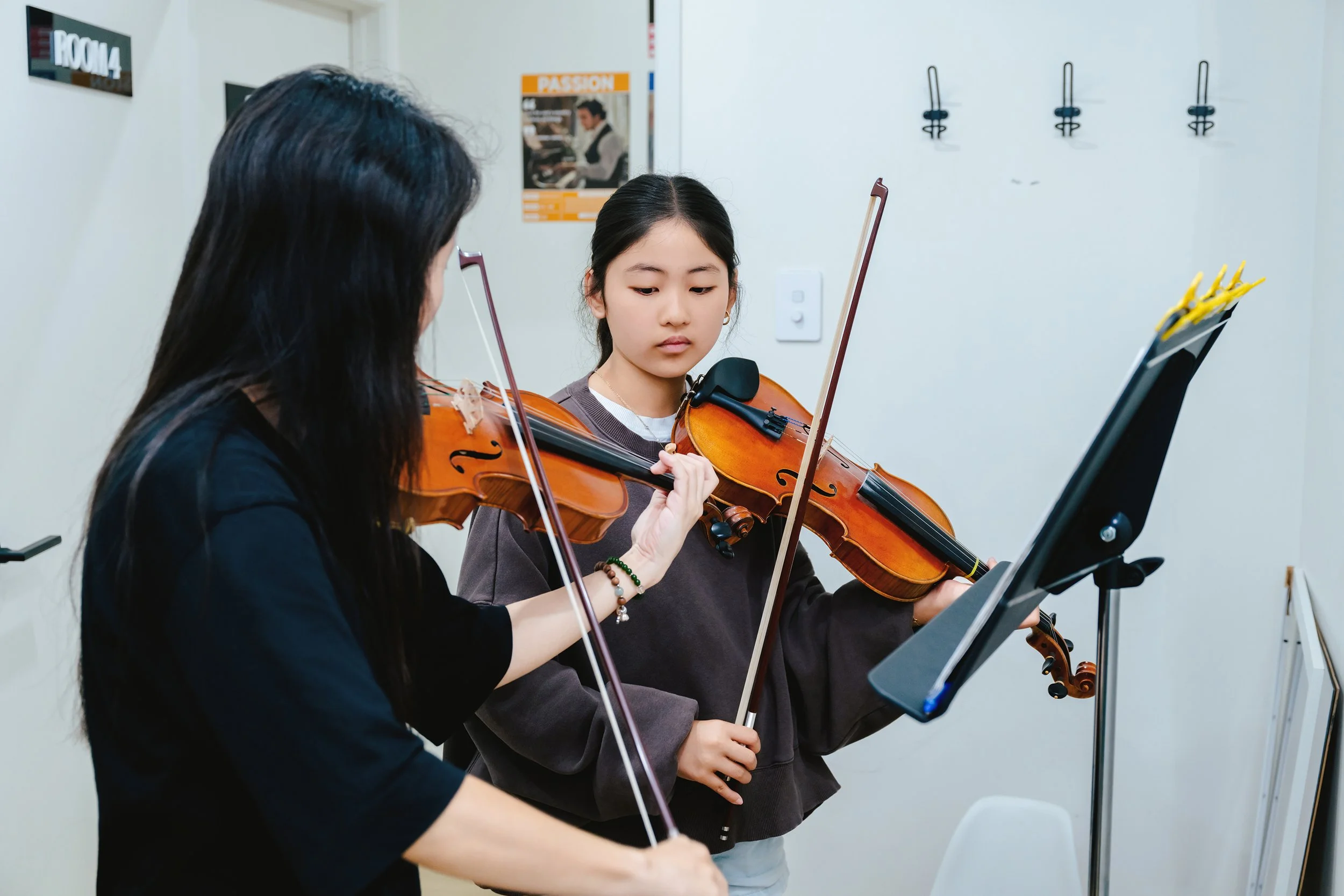 Two girls are playing violins during a music lesson in a classroom.