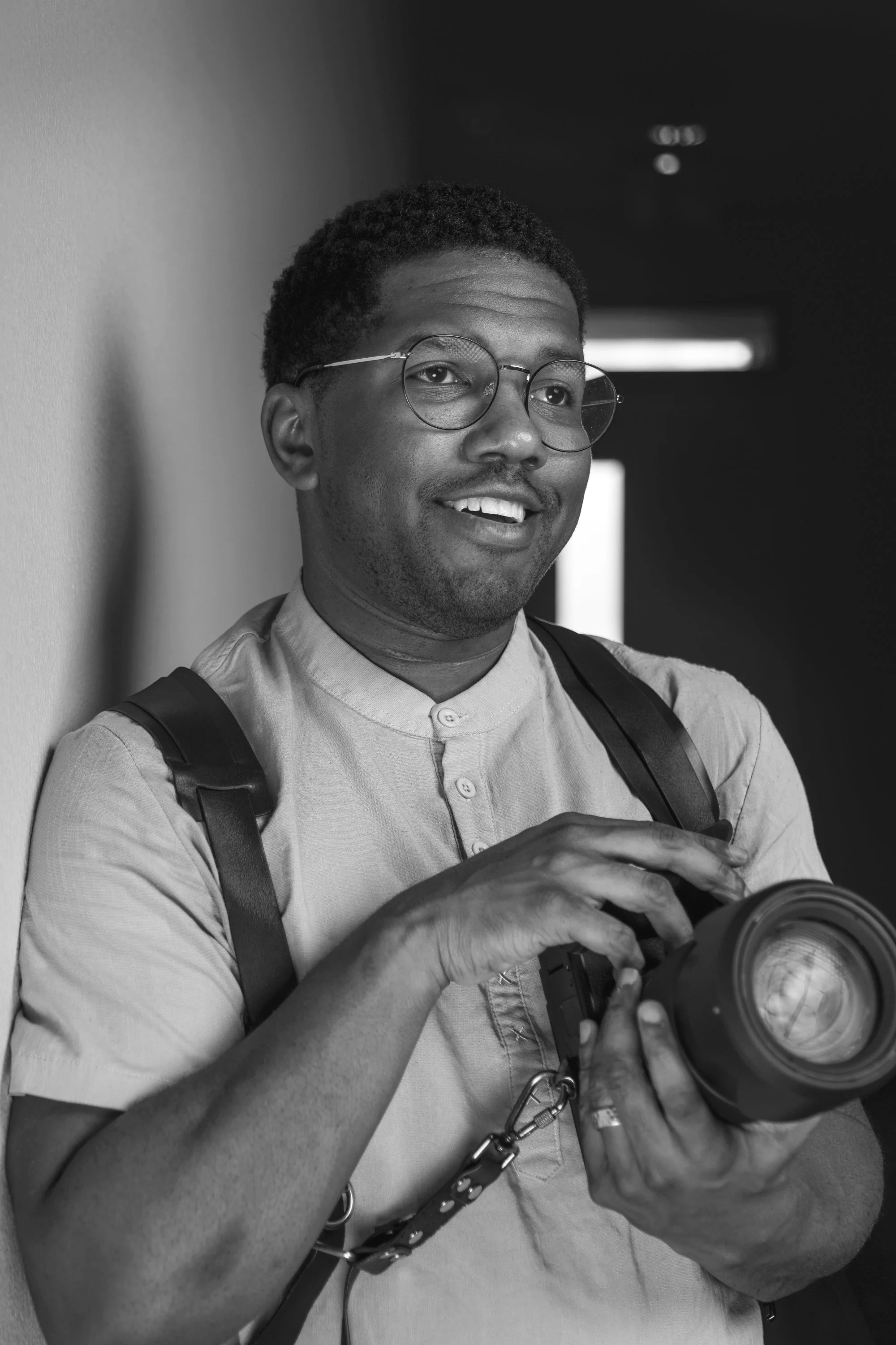 A Dallas photographer with glasses, wearing a button-up shirt, holding a camera and smiling.