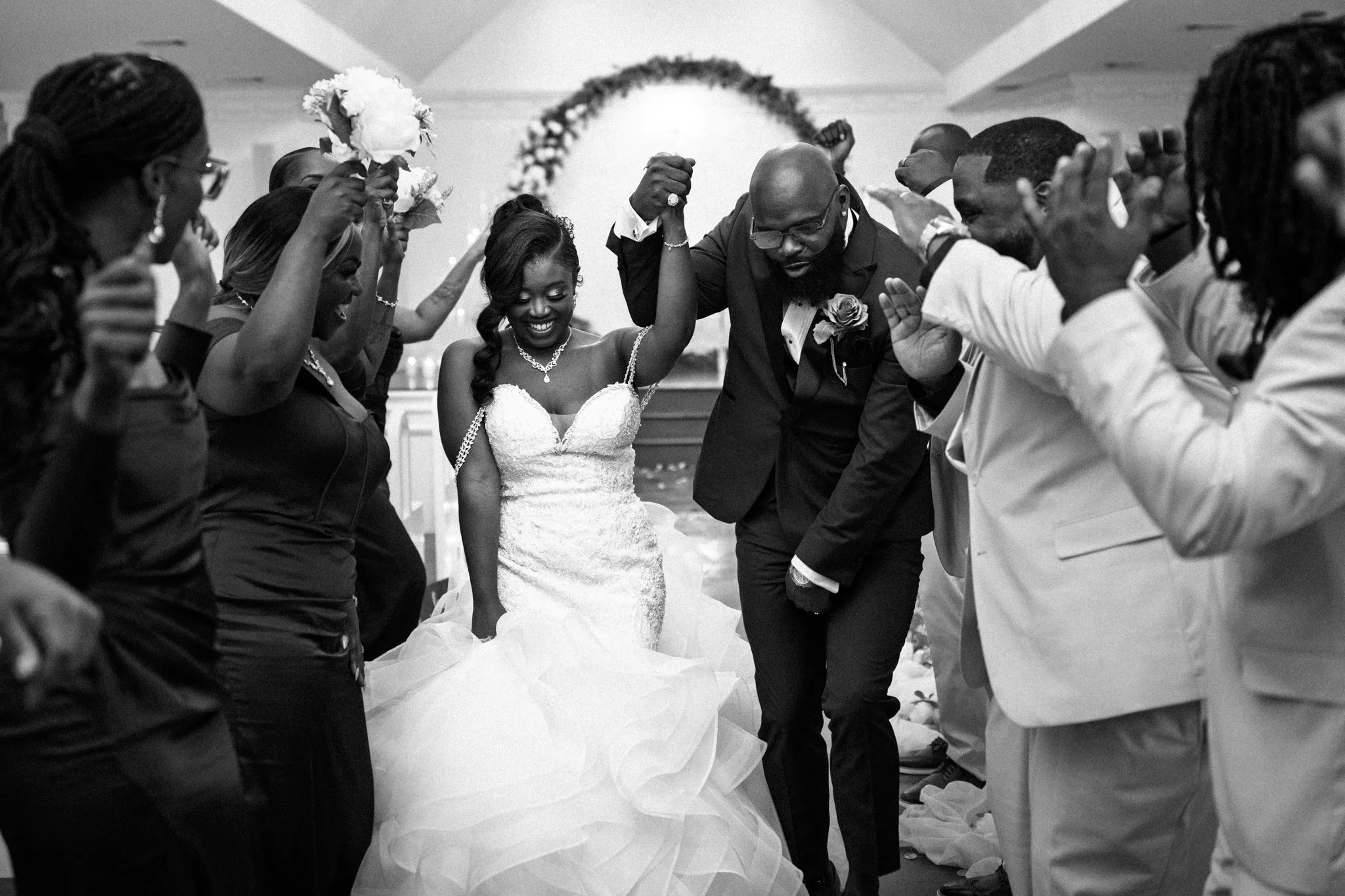 A black-and-white photo of a DFW bride and groom dancing surrounded by friends and family at their wedding reception.
