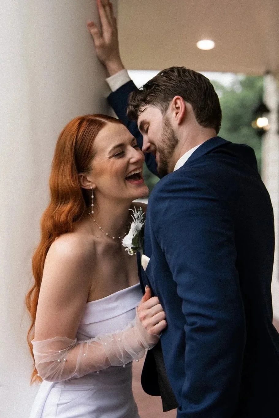 A Dallas bride and groom sharing a joyful moment at their wedding, with the bride wearing a strapless white dress and the groom in a navy suit, standing closely and smiling.