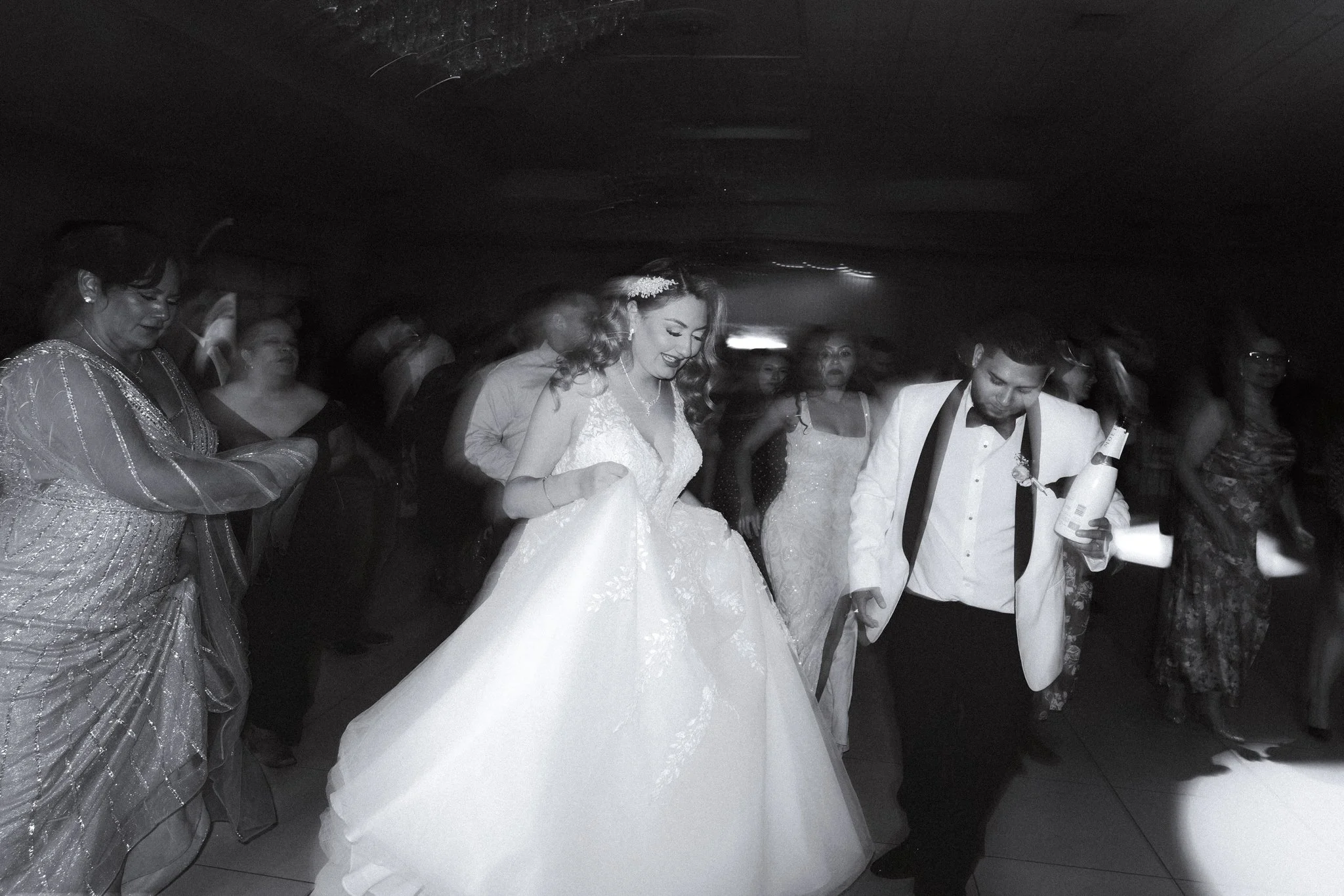 A DFW bride in a wedding gown smiling as she dances at her wedding reception, surrounded by guests in formal attire.