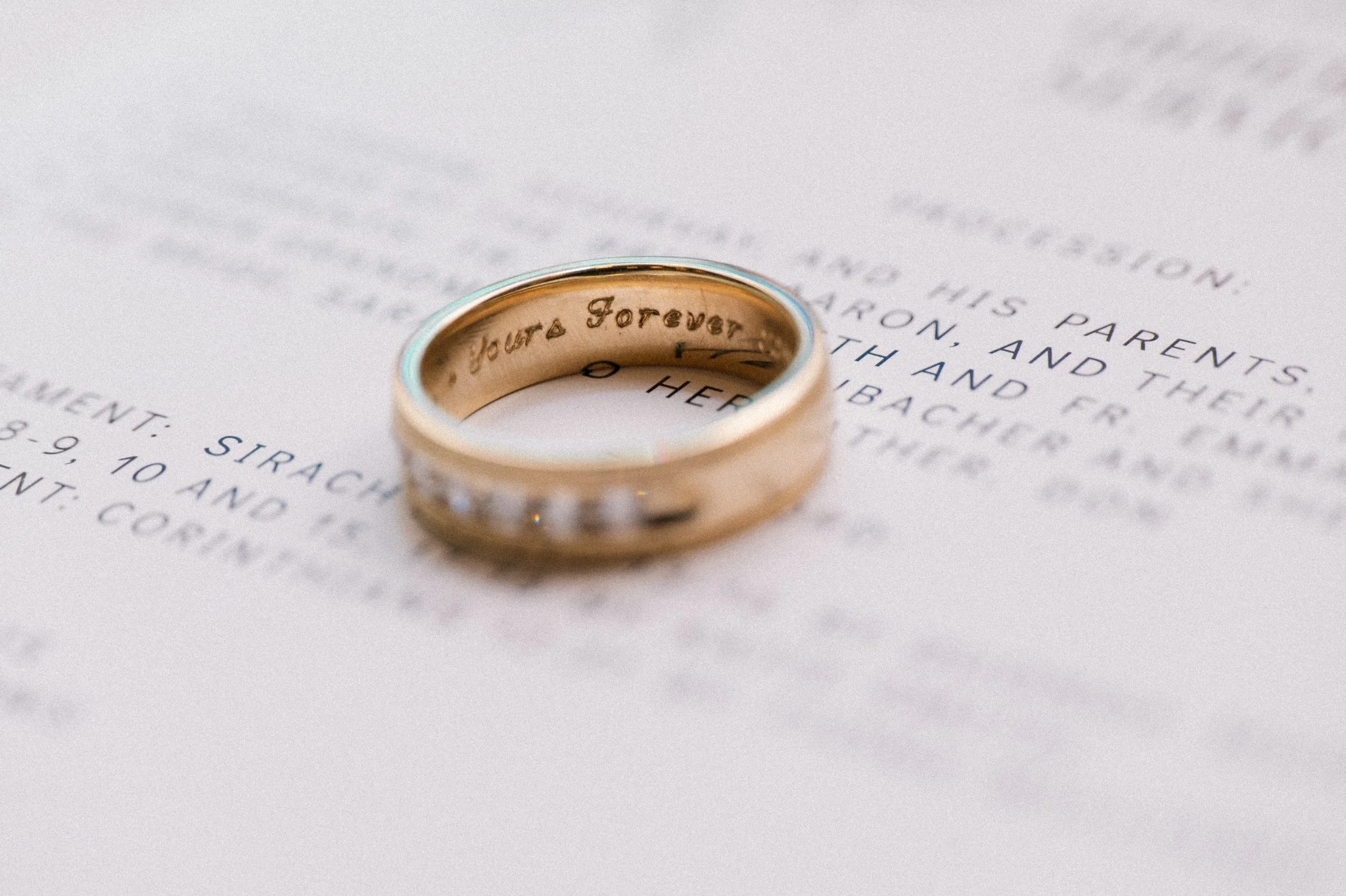 A gold wedding band with the engraved inscription 'Forever Yours' resting on a handwritten note.