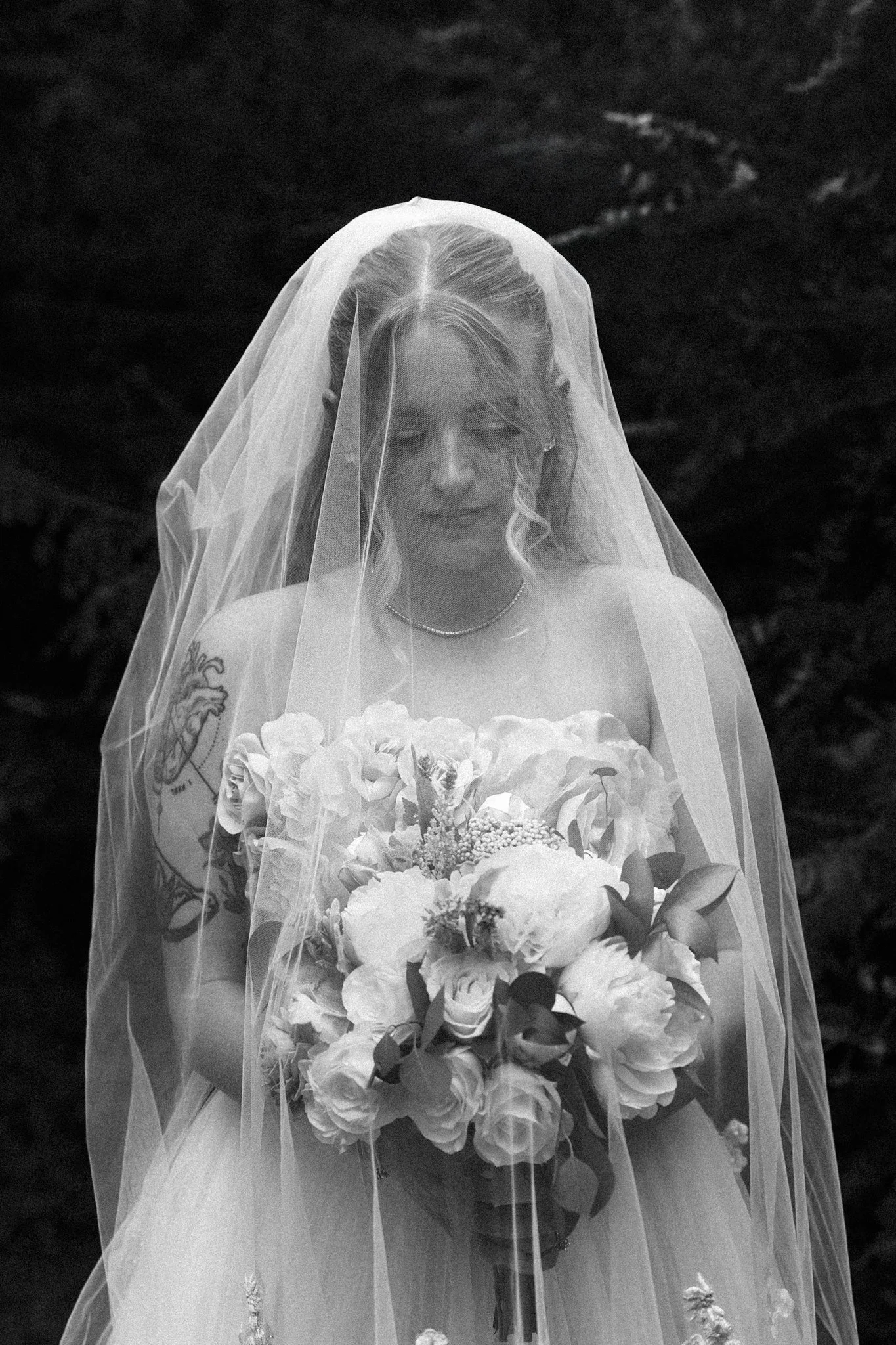 A Dallas bride, wearing a veil and holding a bouquet of flowers, smiling with her eyes closed against a dark background.
