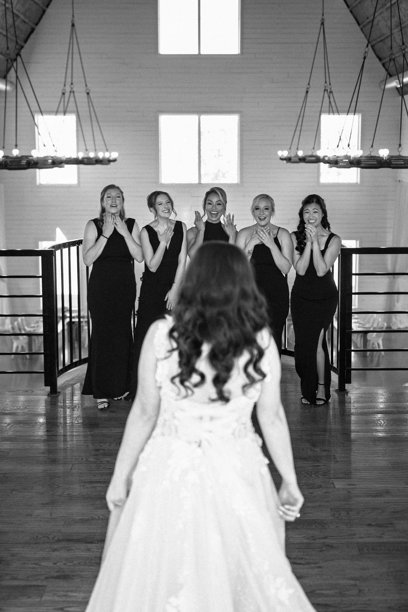 A DFW bride in a wedding dress walking toward five bridesmaids in elegant dresses who are smiling and reacting happily.