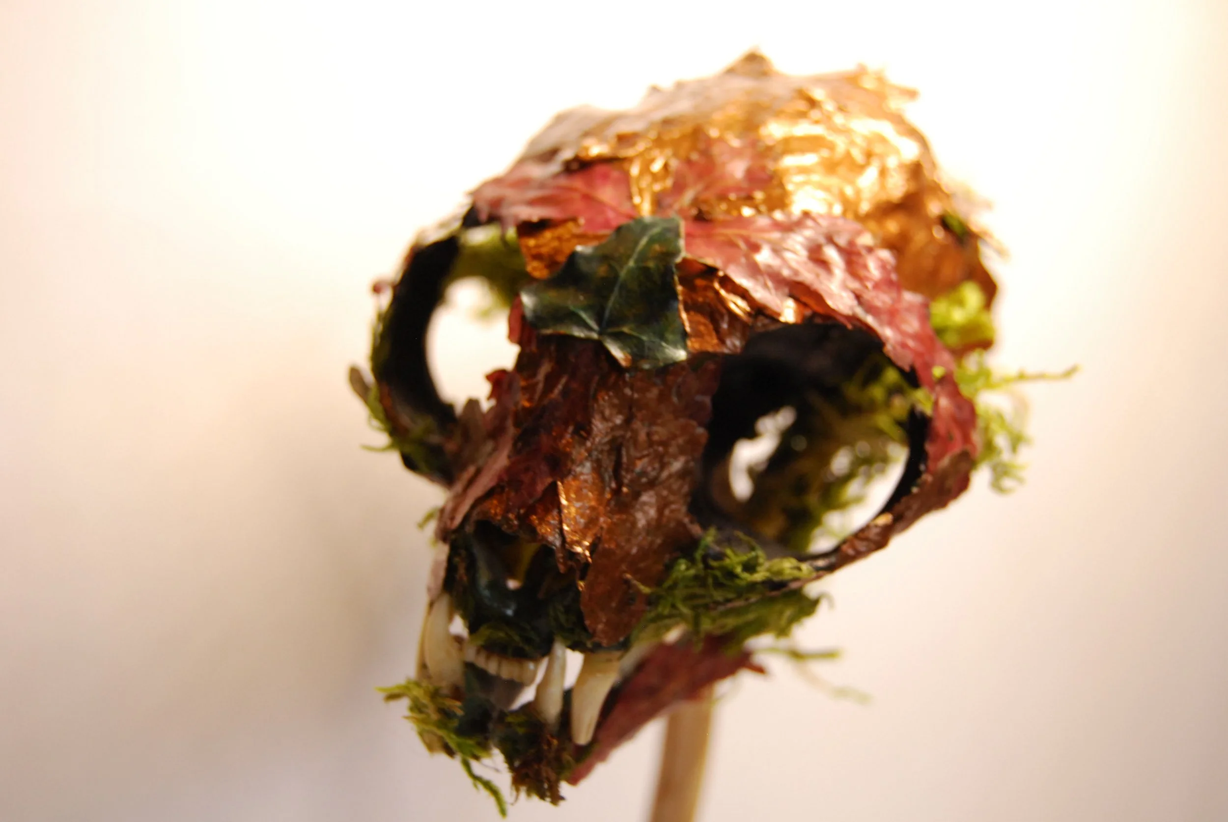 A Halloween pumpkin decoration made from a carved pumpkin with dried autumn leaves, moss, and dark branches, arranged to resemble a spooky face.