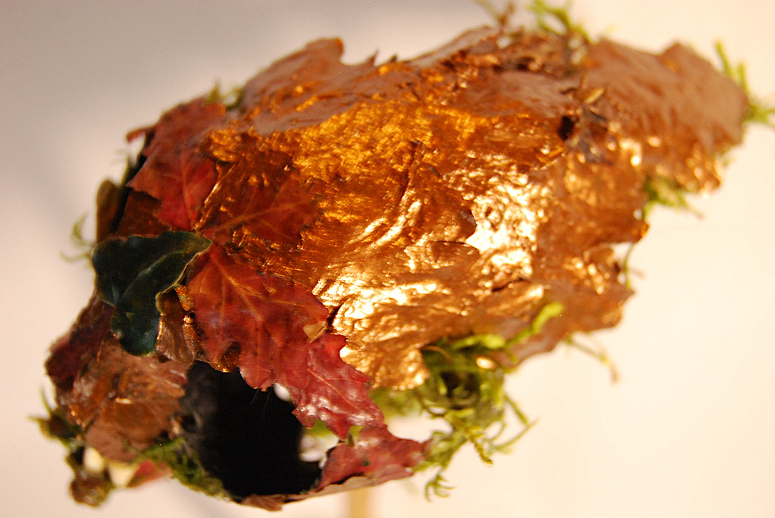 A metallic sculpture of a human face with a smooth, reflective surface and segmented details, mounted on a stand.