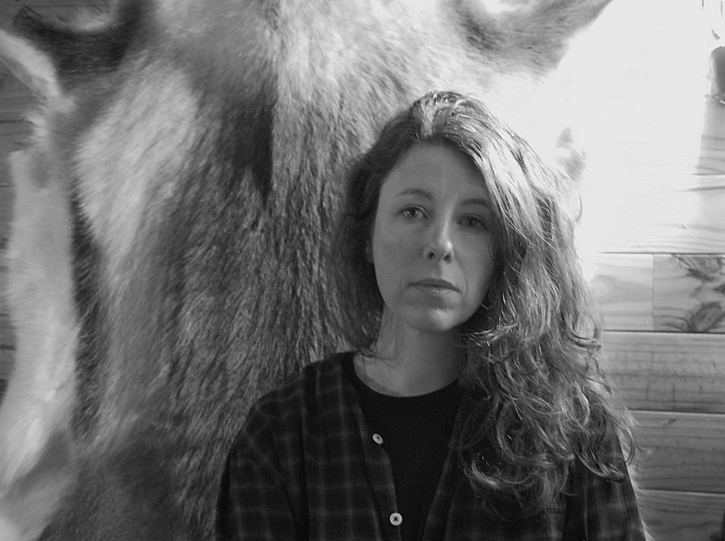 A woman with curly hair and a checkered shirt, indoors with wooden wall paneling.