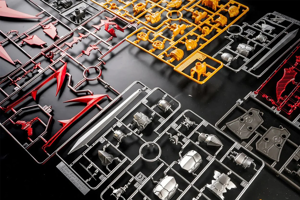 A collection of colorful plastic model parts on sprues arranged on a black surface, including red, yellow, silver, and black pieces.