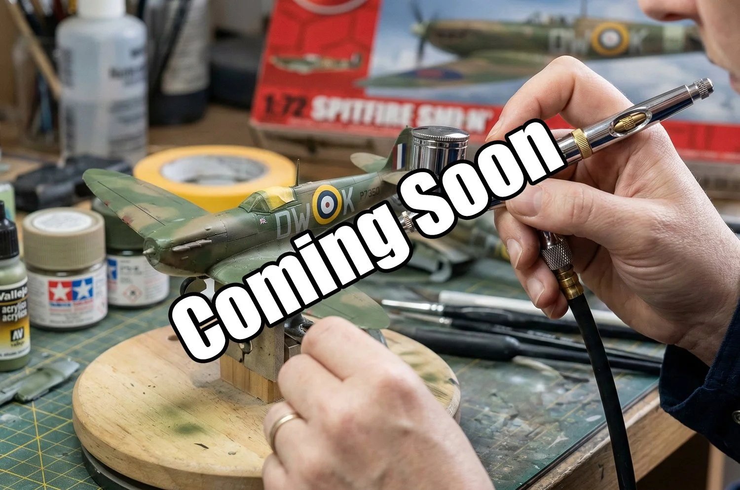 Person working on a detailed model airplane, using an airbrush to paint a camouflage pattern.