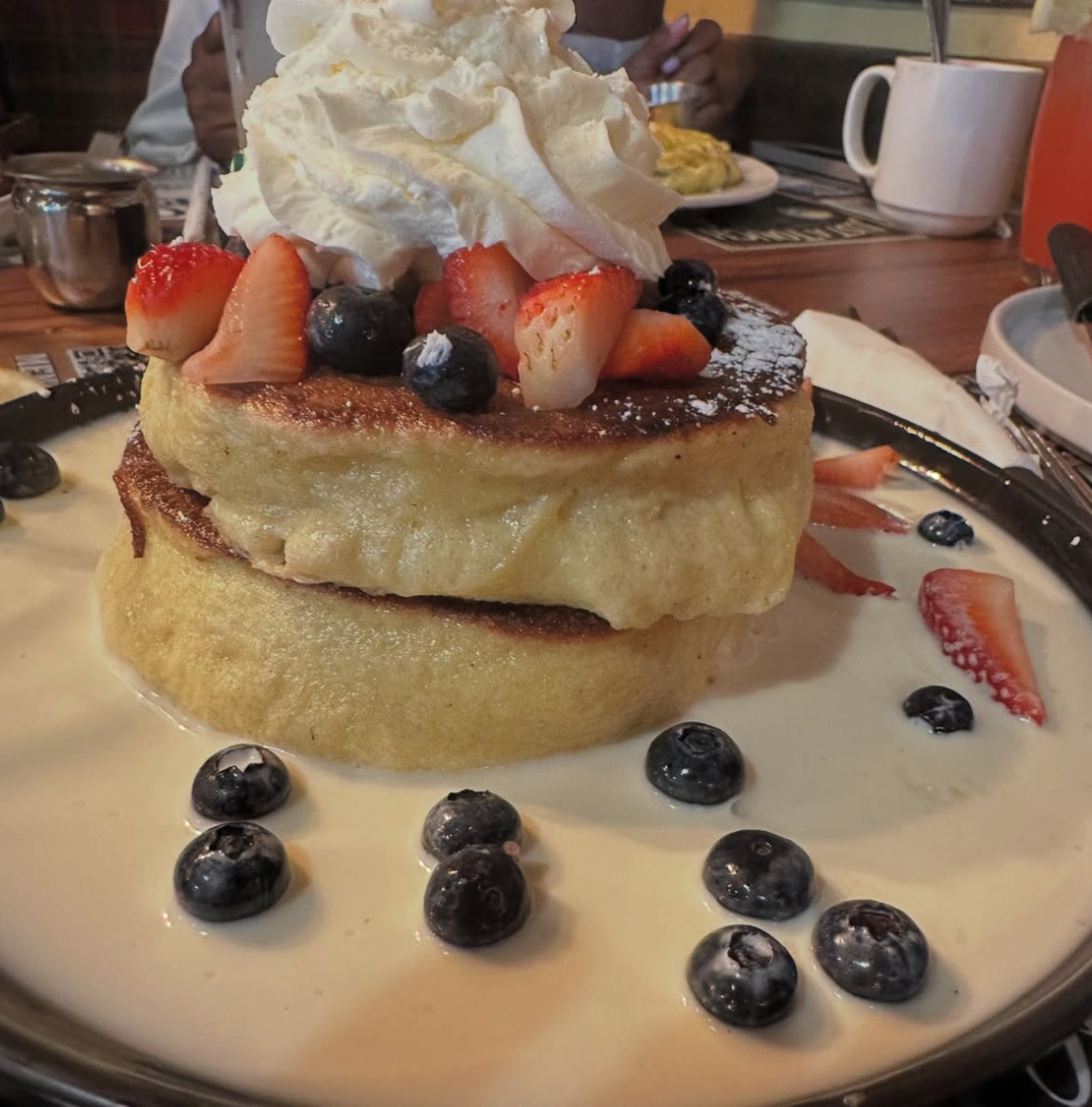 Stack of two thick slices of French toast topped with whipped cream, fresh strawberries and blueberries, dusted with powdered sugar, and surrounding the toast with more berries in a creamy sauce.