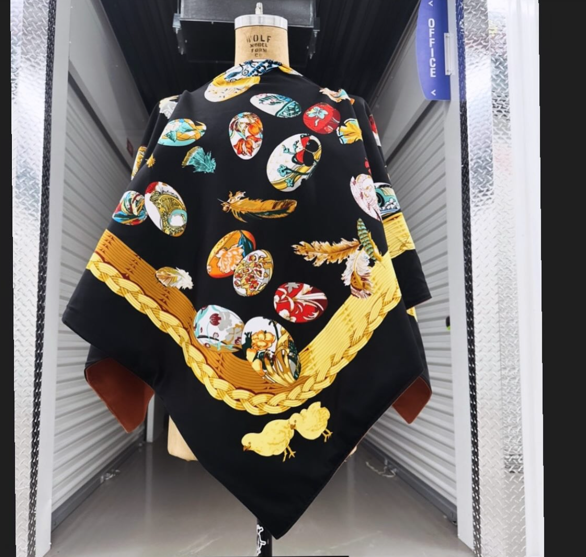 A black silk scarf with a pattern of colorful decorative Easter eggs, surrounded by a thick yellow rope design, and two yellow chicks at the bottom.