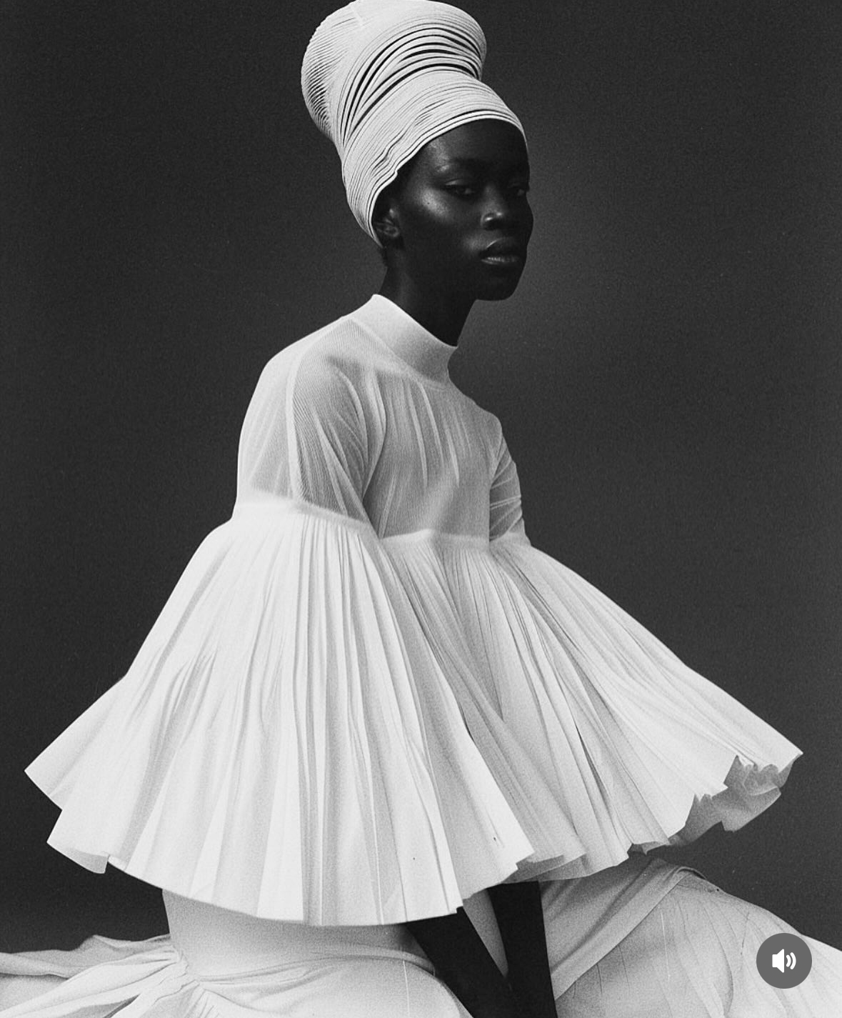A black-and-white photo of a woman with dark skin wearing a white, pleated, layered dress and a headwrap, sitting against a plain dark background.