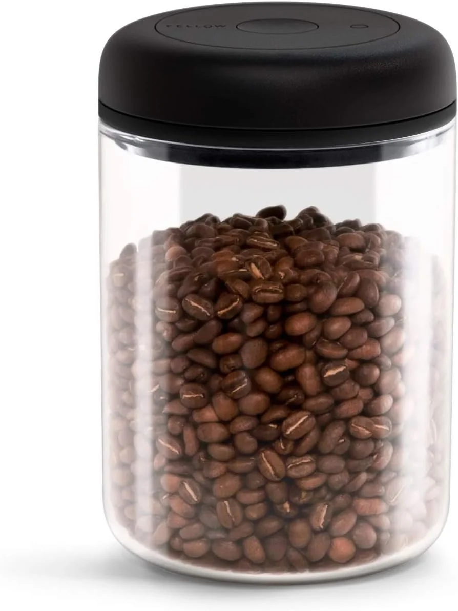 A clear glass jar filled with roasted coffee beans, with a black lid on top.