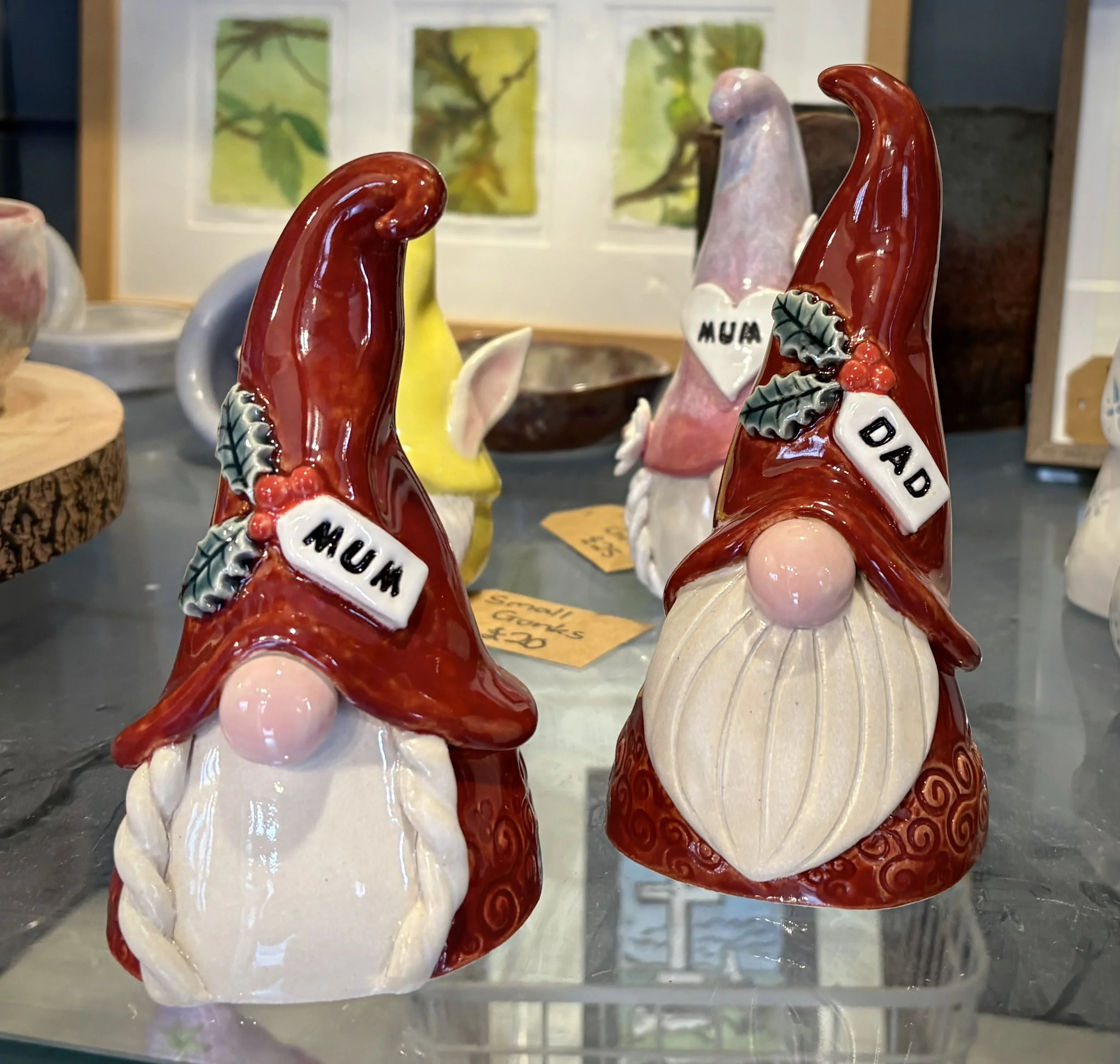 Decorative ceramic garden gnomes with red hats labeled 'MUM' and 'DAD', sitting on a glass display table.