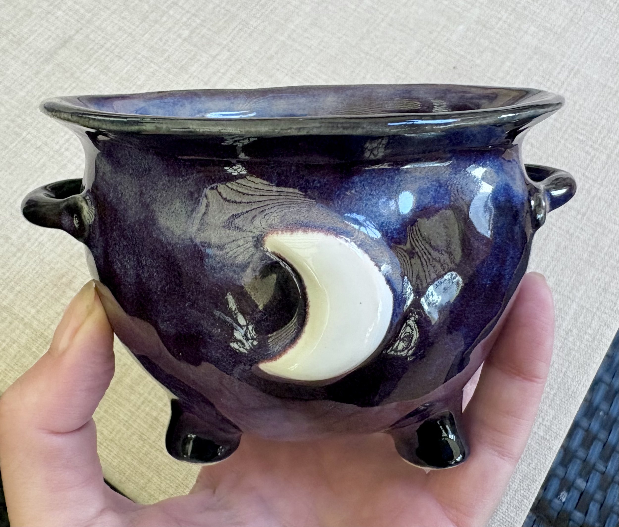 A person is holding a ceramic bowl with a shiny, dark glaze and what appears to be a painted or carved design of a pale moon and abstract patterns.