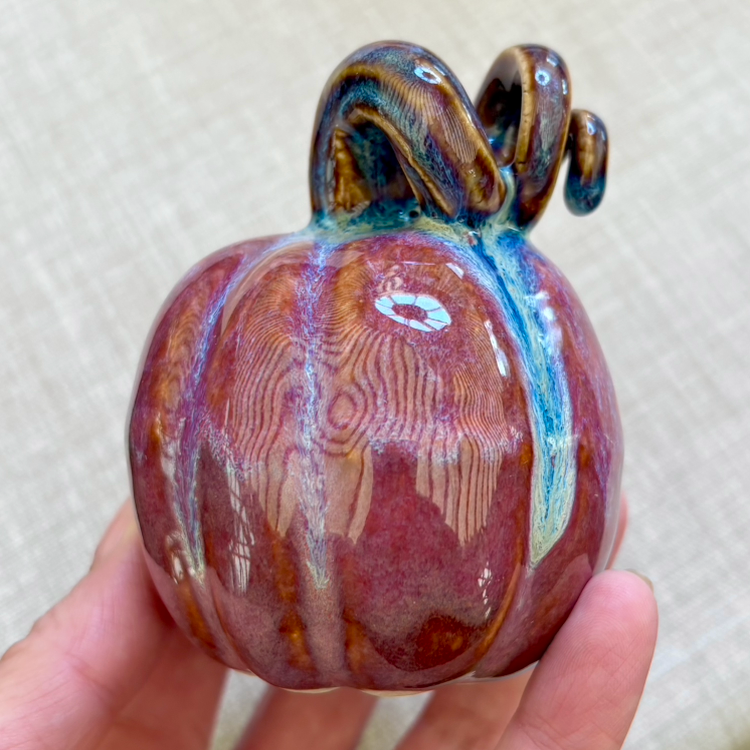 A glass pumpkin with a multicolored, swirling glaze, featuring a twisted glass vine on top.