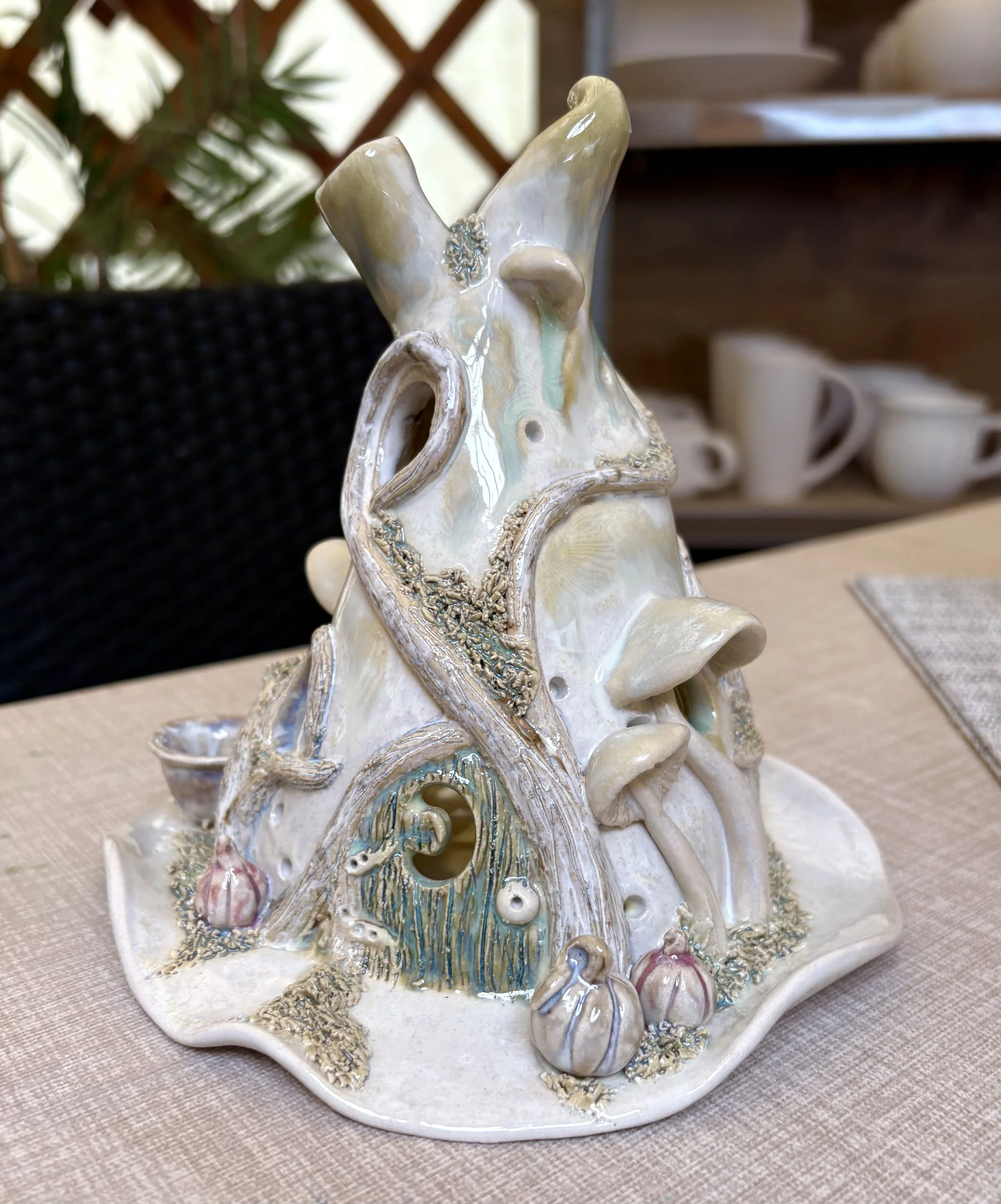 Decorative ceramic sculpture of a fantasy tree house with mushrooms, pumpkins, and vines, on a table.