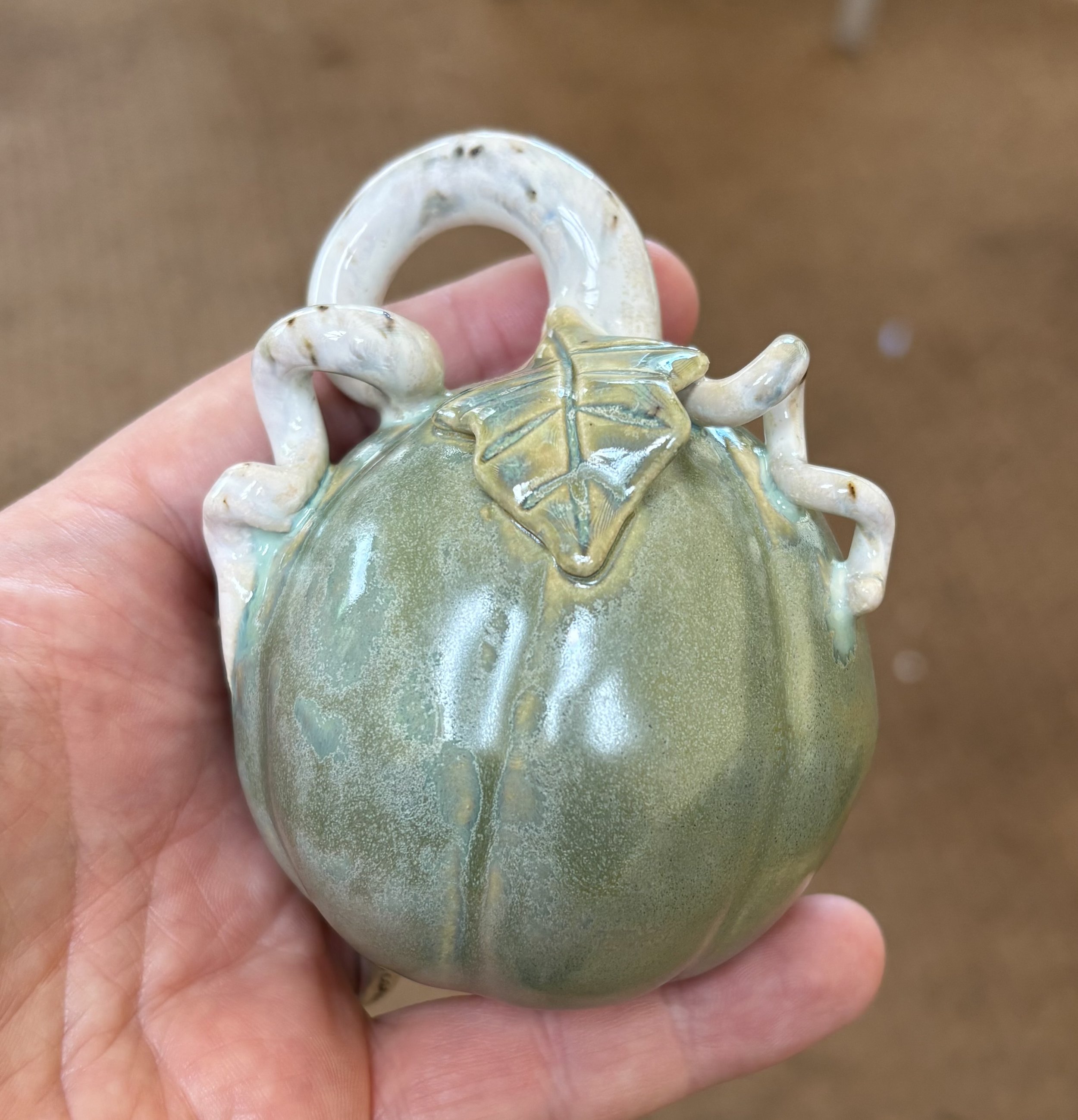 A ceramic pumpkin-shaped vessel with a leaf detail and curling vine handles.