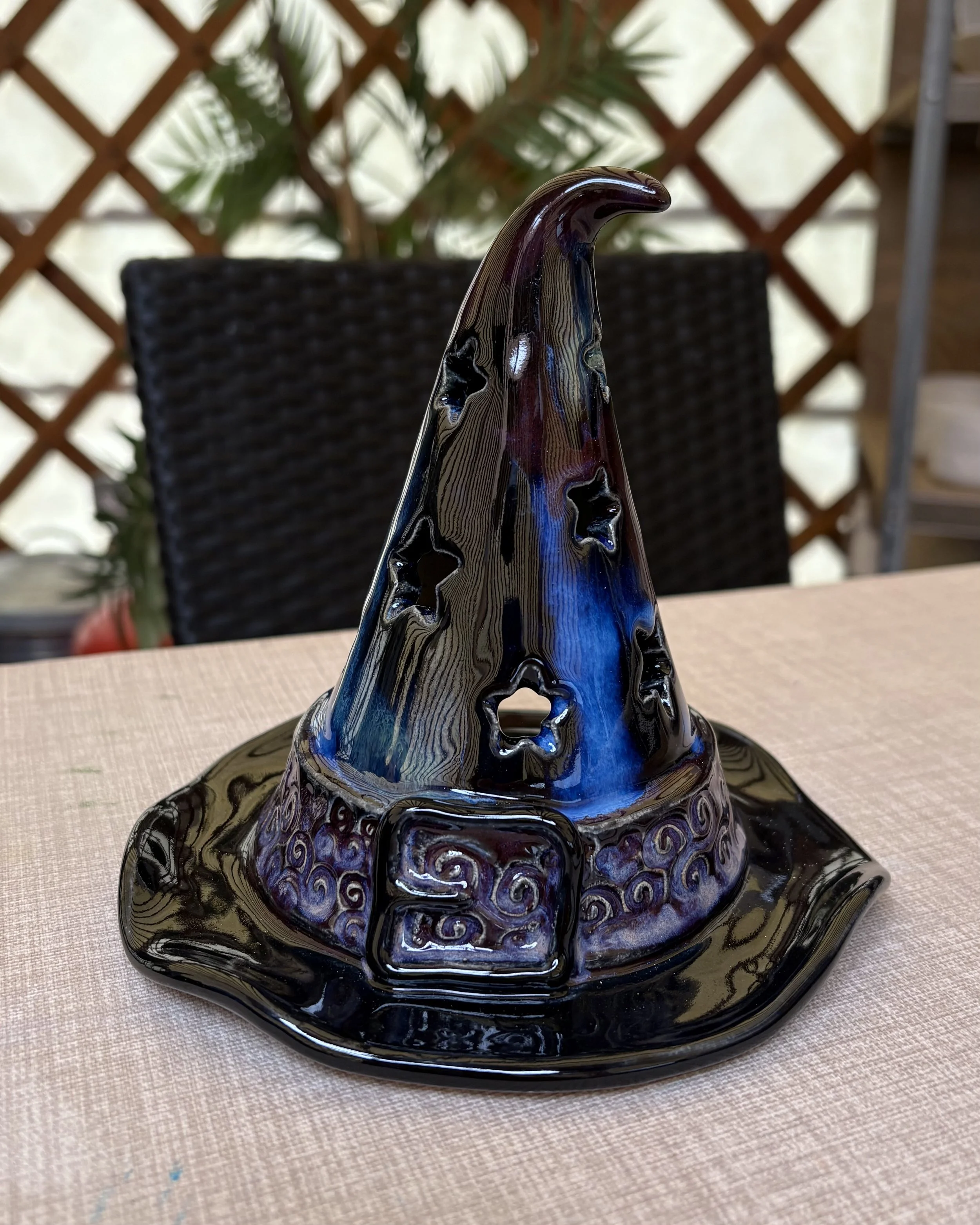 Colorful witch's hat decorative ceramic sculpture with star-shaped cutouts and intricate designs, placed on a table.
