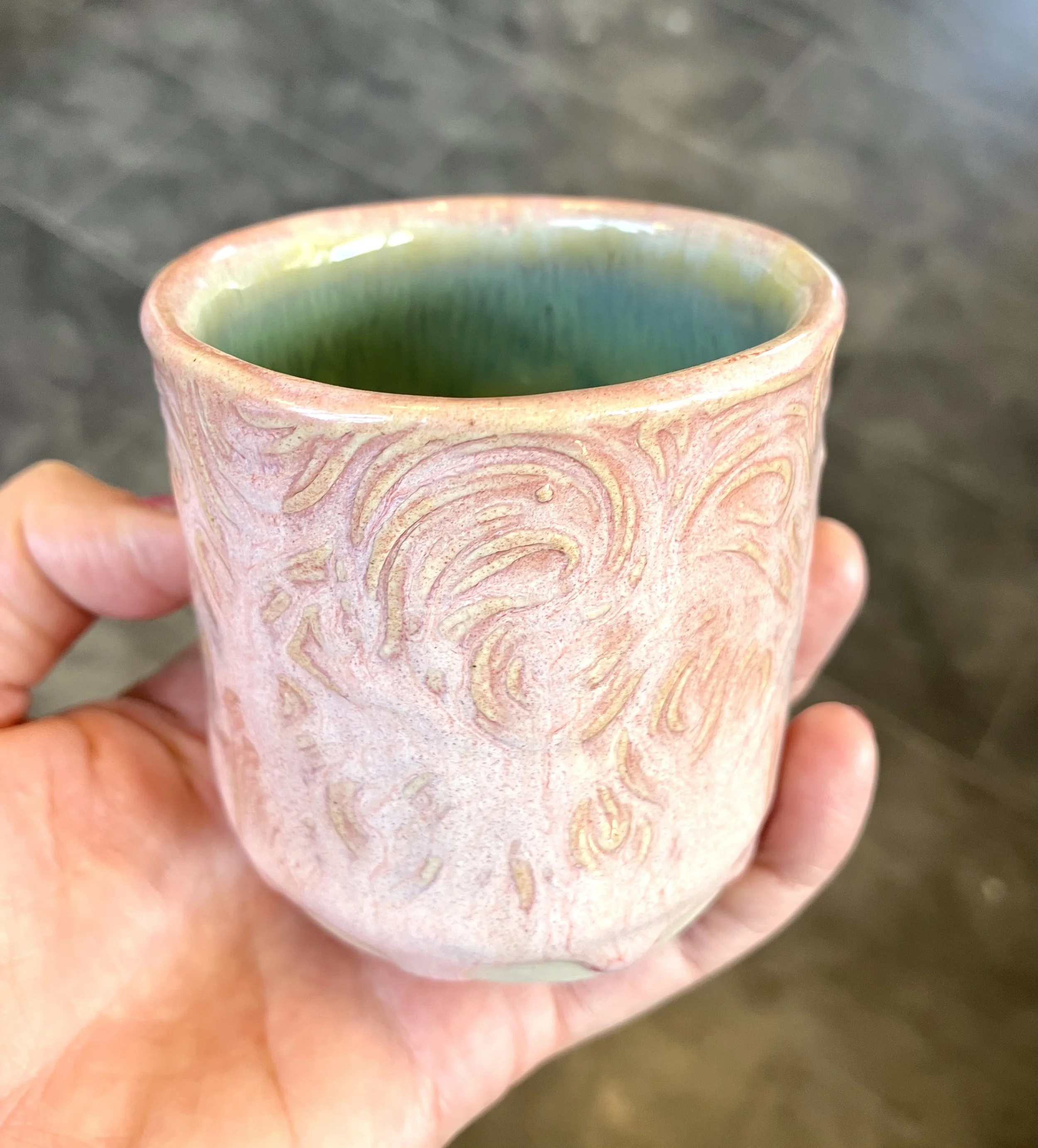Hand holding a pink ceramic mug with swirled patterns and a green and blue interior.