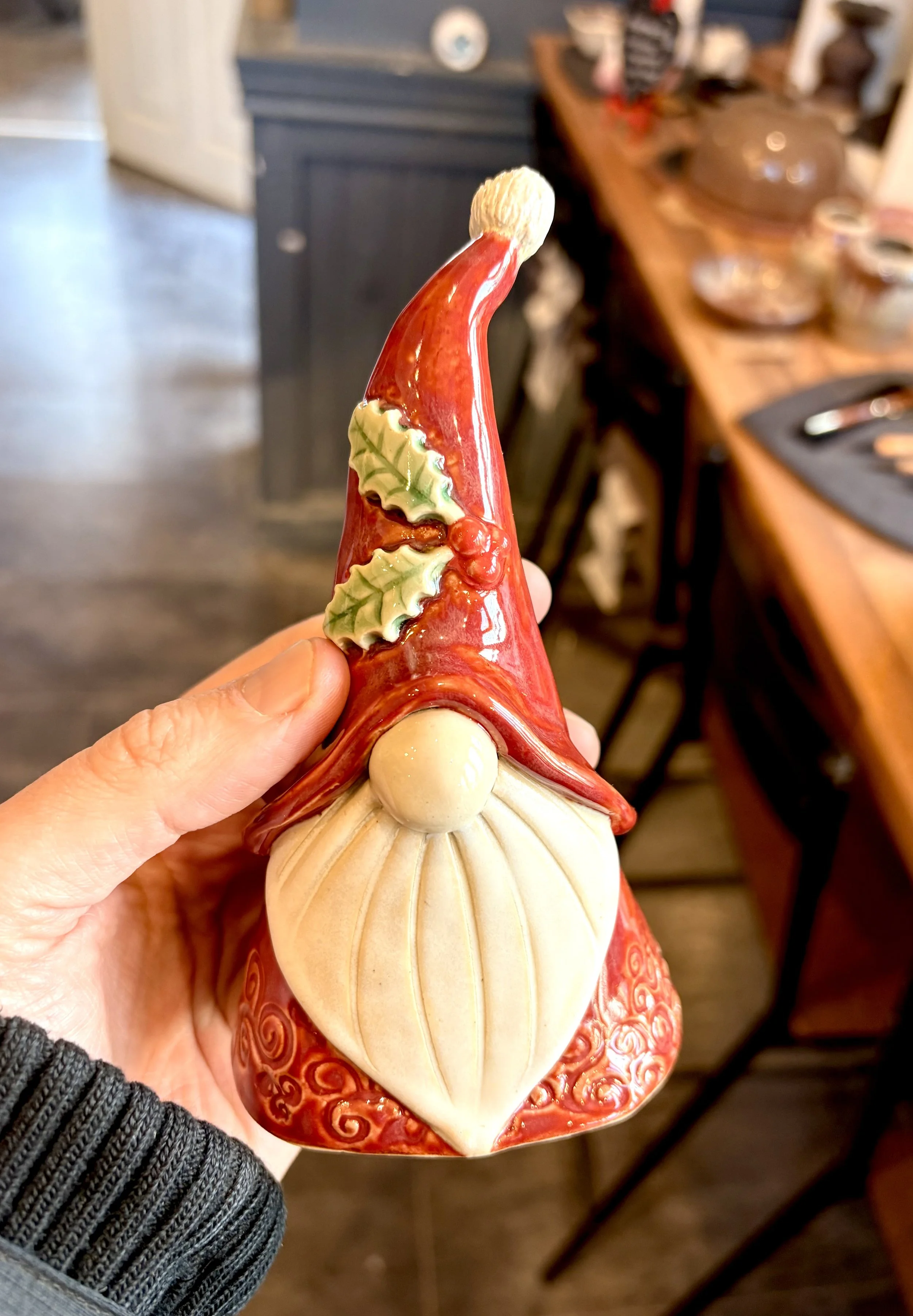 Decorative ceramic Santa Claus figurine with a red hat, holly leaves, and a white beard, held by a person's hand in a cozy home setting.