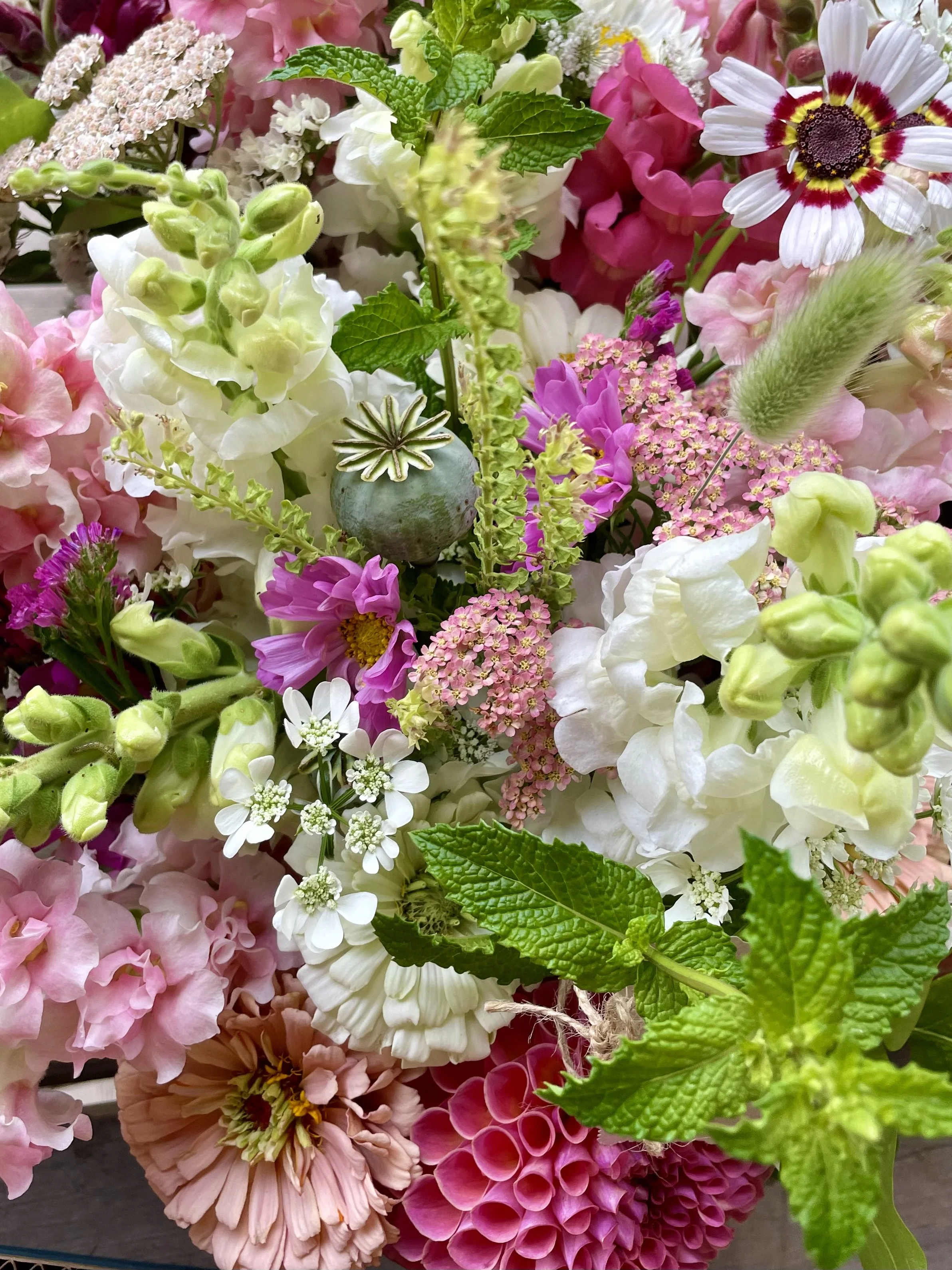 A vibrant bouquet of various flowers including pink, white, purple, and yellow blooms, green leaves, and different textures.
