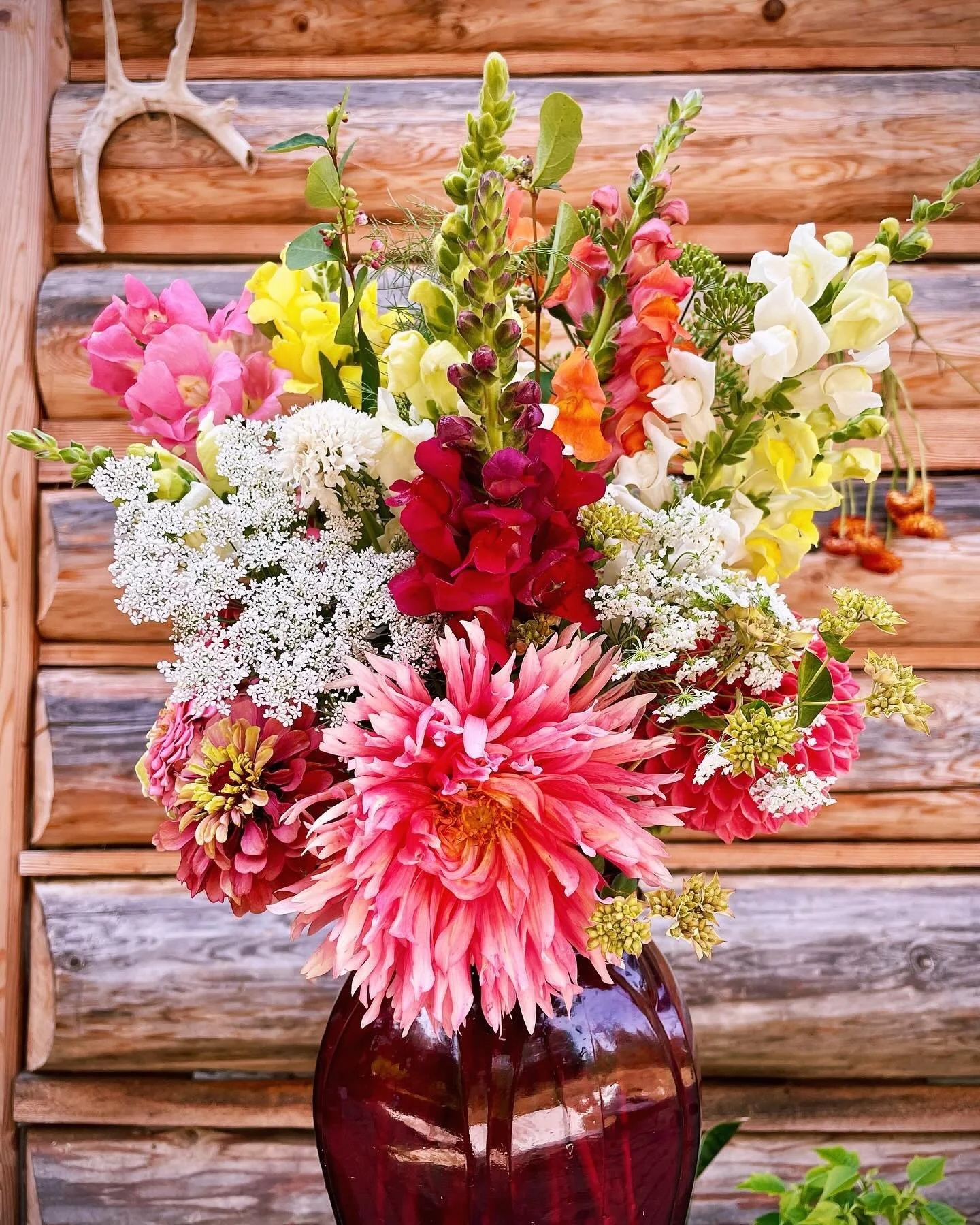 A colorful bouquet of various flowers in a dark red vase with a wooden background.