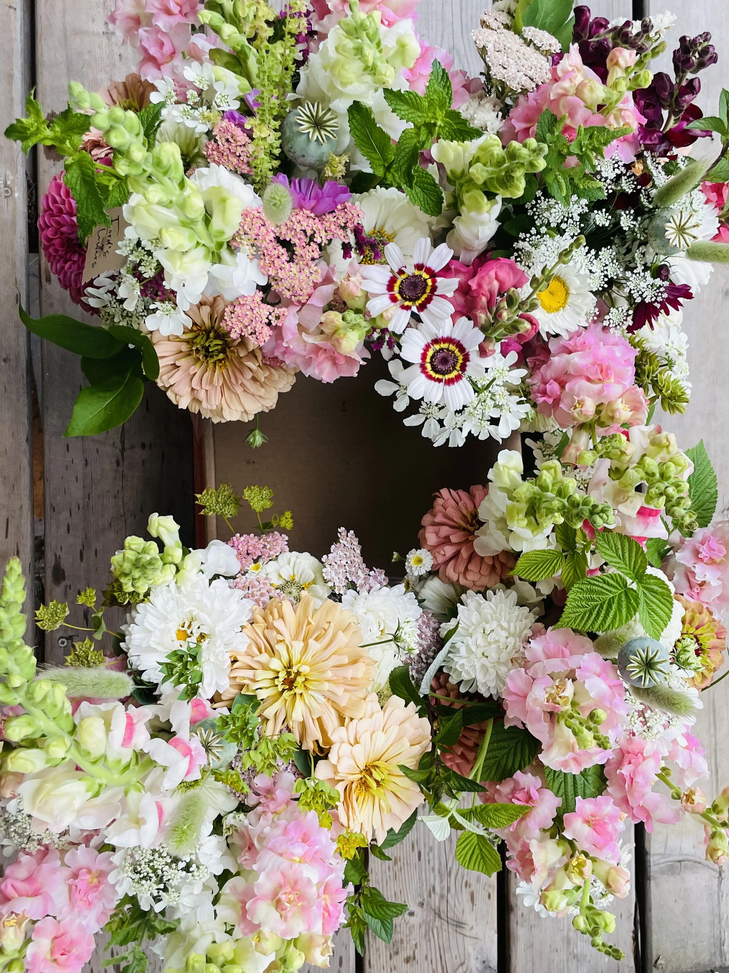 A colorful floral wreath made of various pink, white, peach, and purple flowers arranged on a wooden surface.