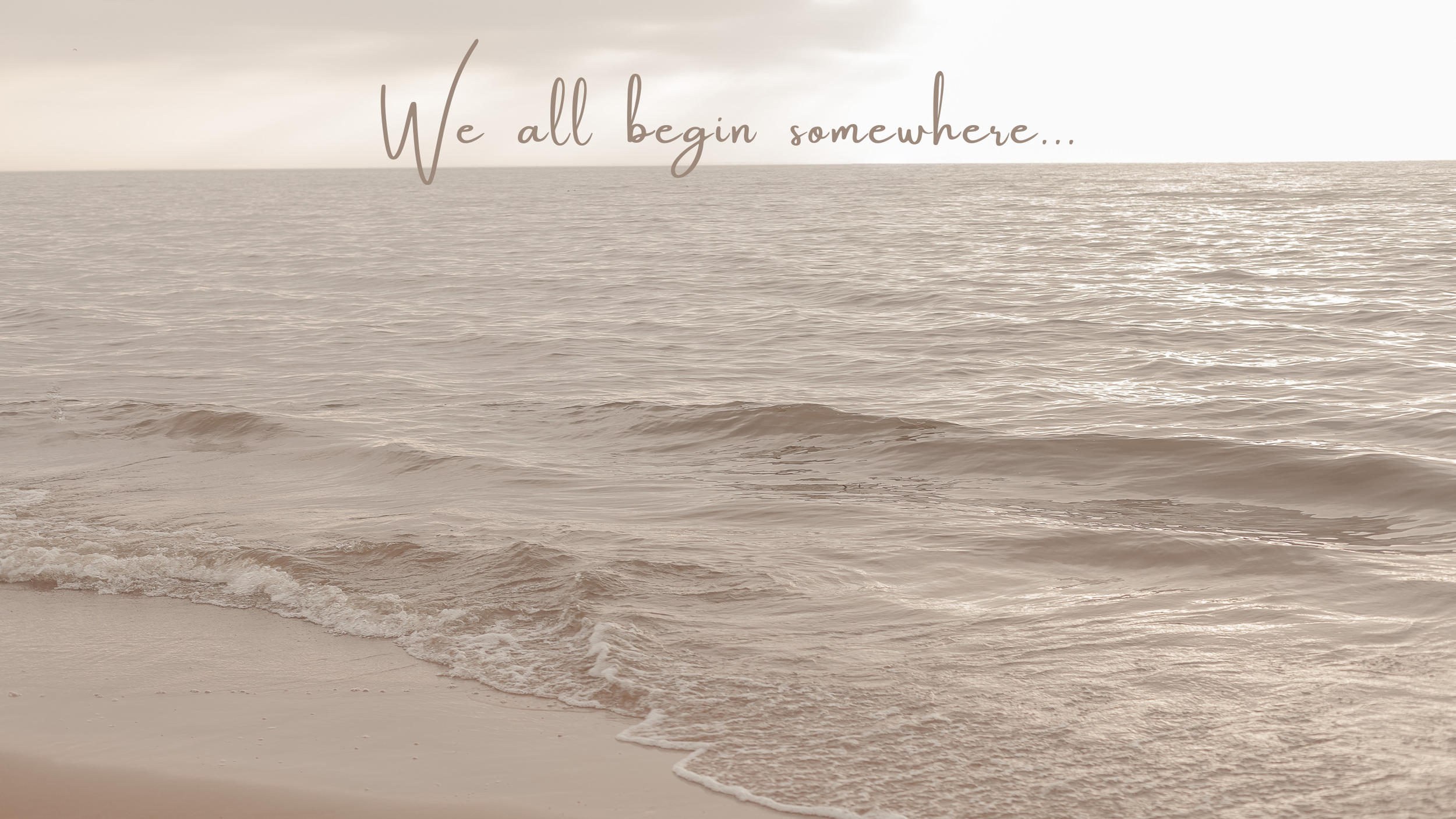 A serene beach scene with gentle waves lapping at the sand, overlaid with the quote "We all begin somewhere..." in elegant script.