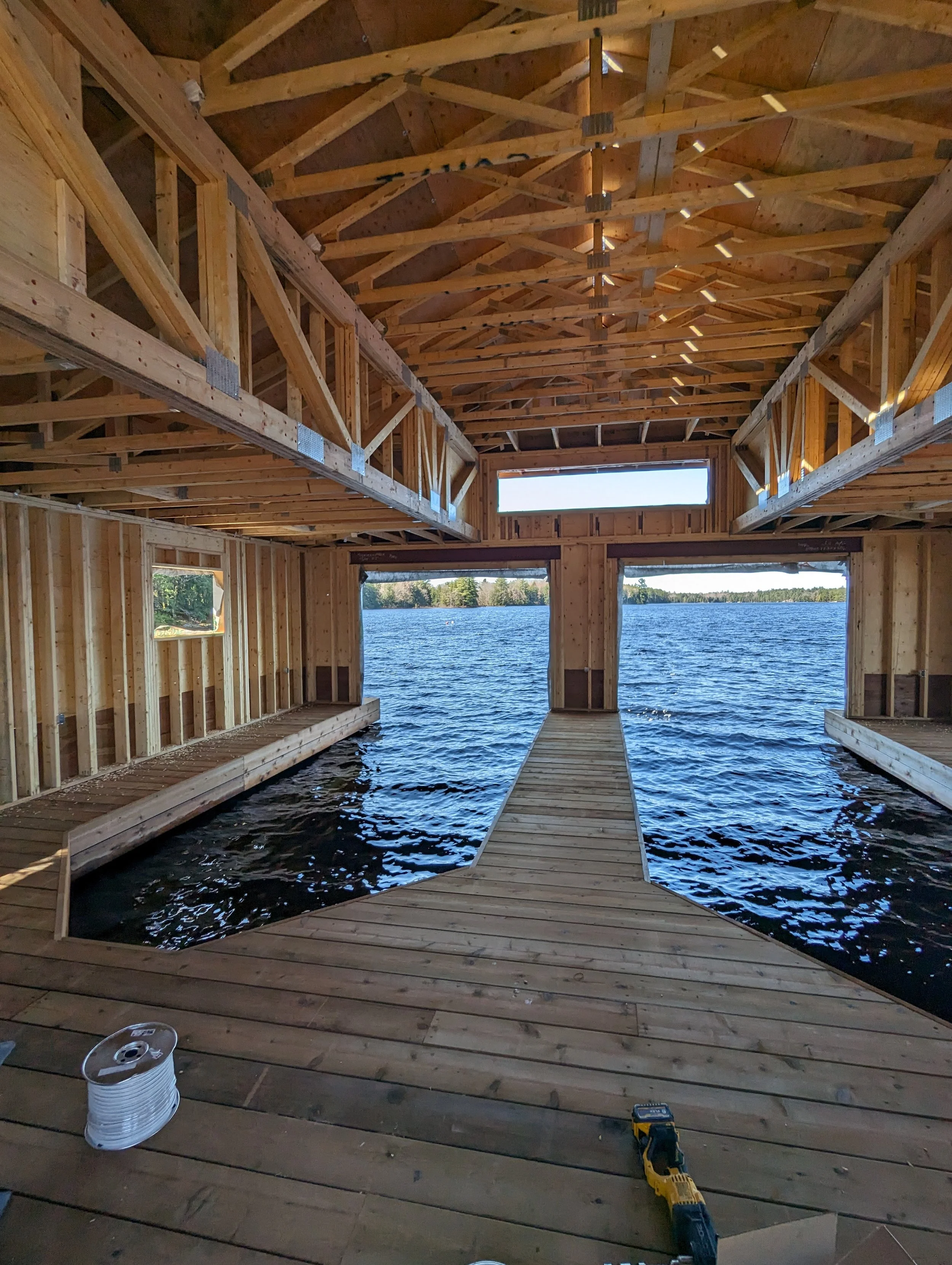 Under construction boathouse with wooden framework and a water view, showing the interior structure, floor, and opening to a lake.